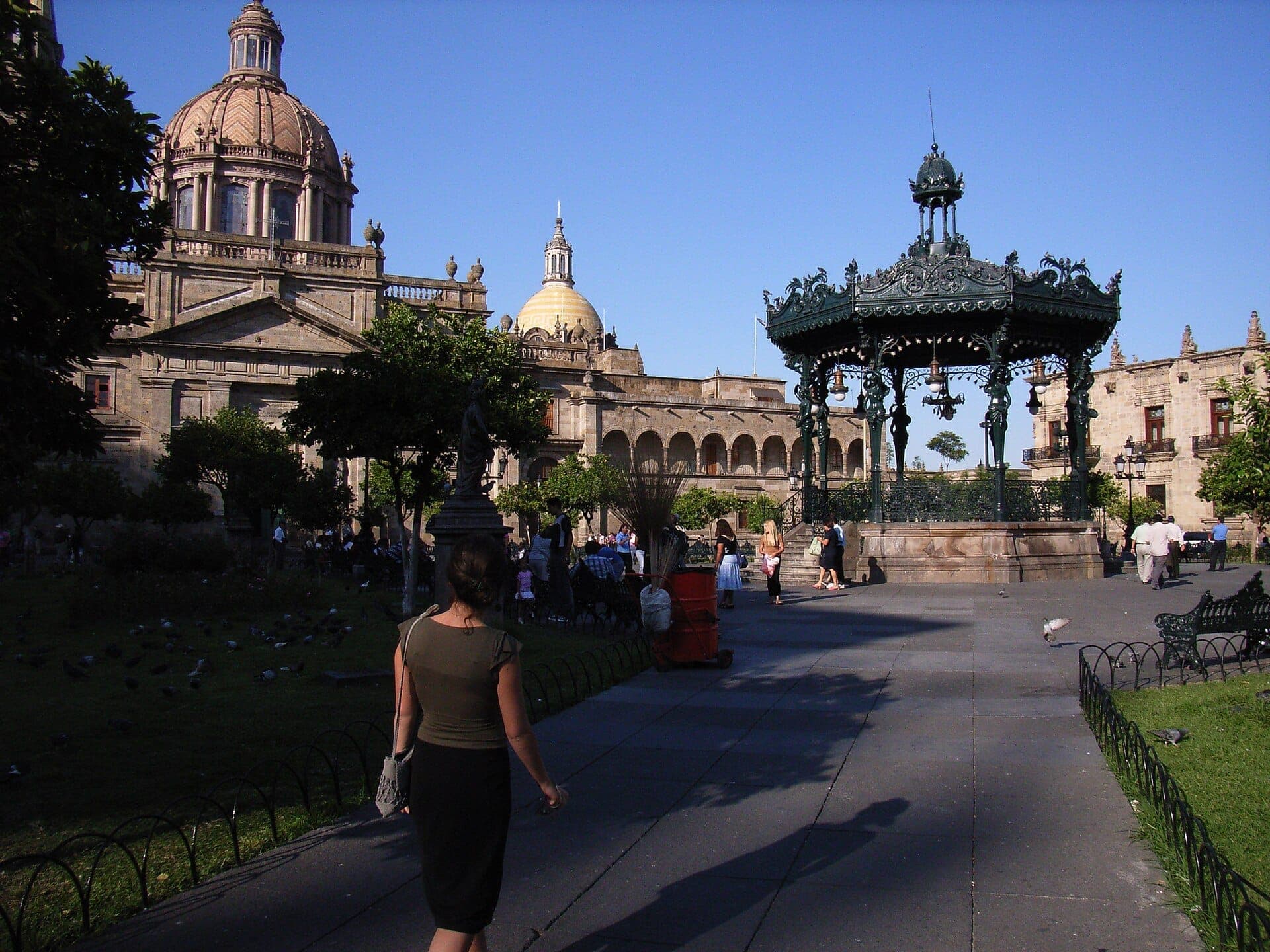Plaza de Armas Guadalajara พร้อมศาลาดนตรีสไตล์อาร์ตนูโวของฝรั่งเศสที่華丽งดงาม โดมอาสนวิหาร ต้นไม้สีเขียวโดยรอบ และผู้คนที่สนุกสนานในบ่ายวันแดดจ้า