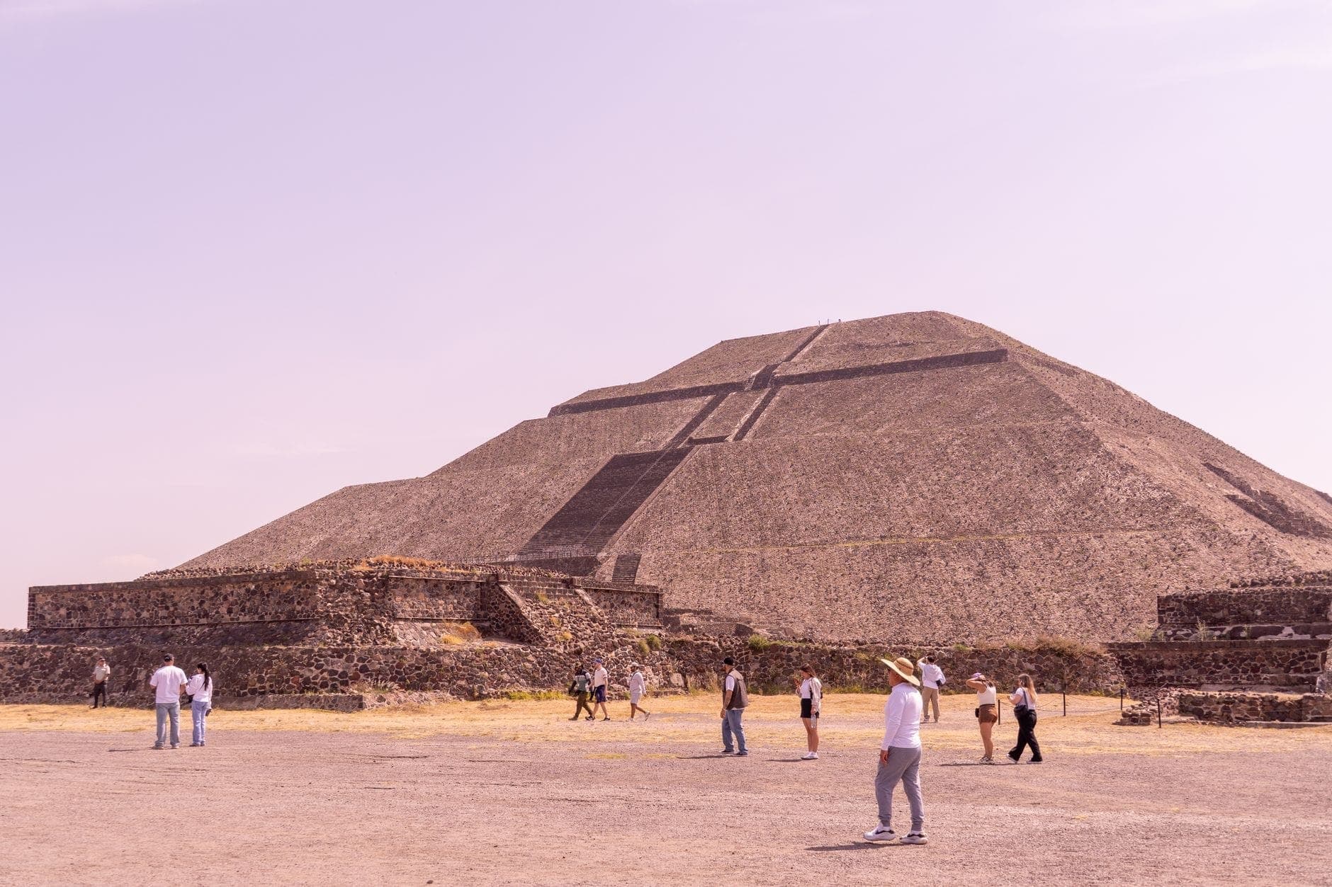 ภาพมุมกว้างของพีระมิดแห่งดวงอาทิตย์ที่ Teotihuacan ท่ามกลางท้องฟ้าโปร่ง มีนักท่องเที่ยวเดินอยู่เบื้องหน้า โชว์สัดส่วนอันยิ่งใหญ่ของโบราณสถาน