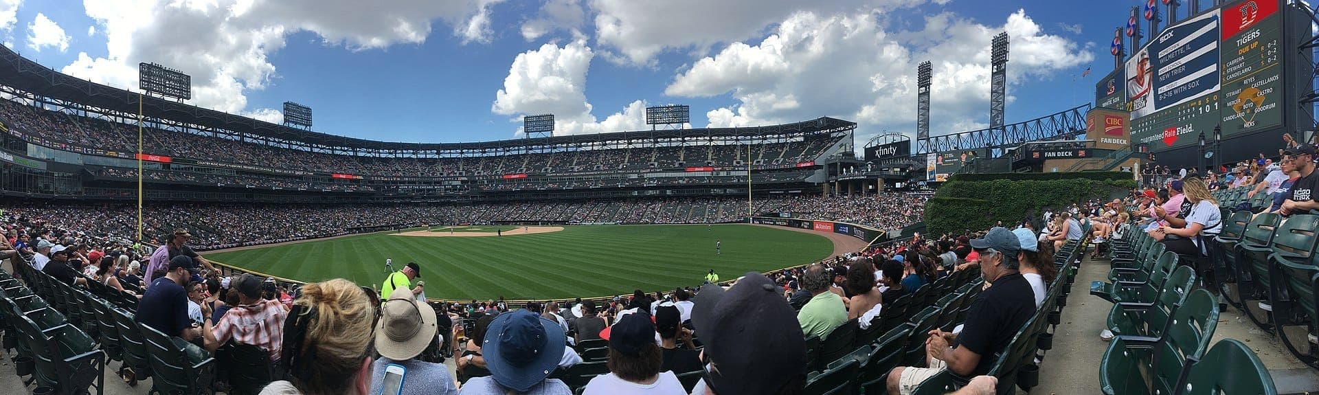 Panoramic view of Rate Field during a daytime baseball game, packed stands, lush green field, and clear blue skies with scattered clouds.