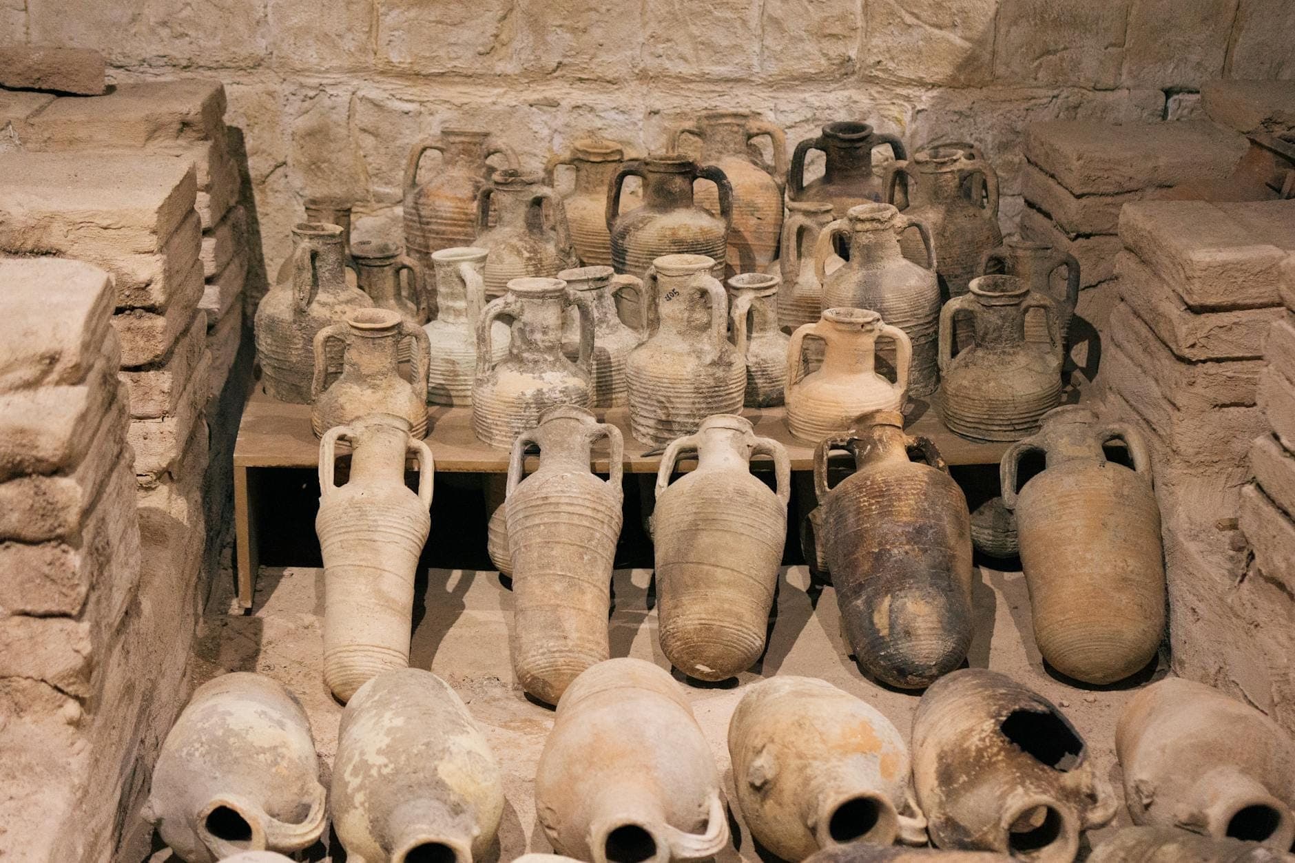 Ausstellung zahlreicher antiker minoischer Tonamphoren und Keramikgefäße, auf Regalen vor einer Steinwand in einem archäologischen Museum arrangiert.