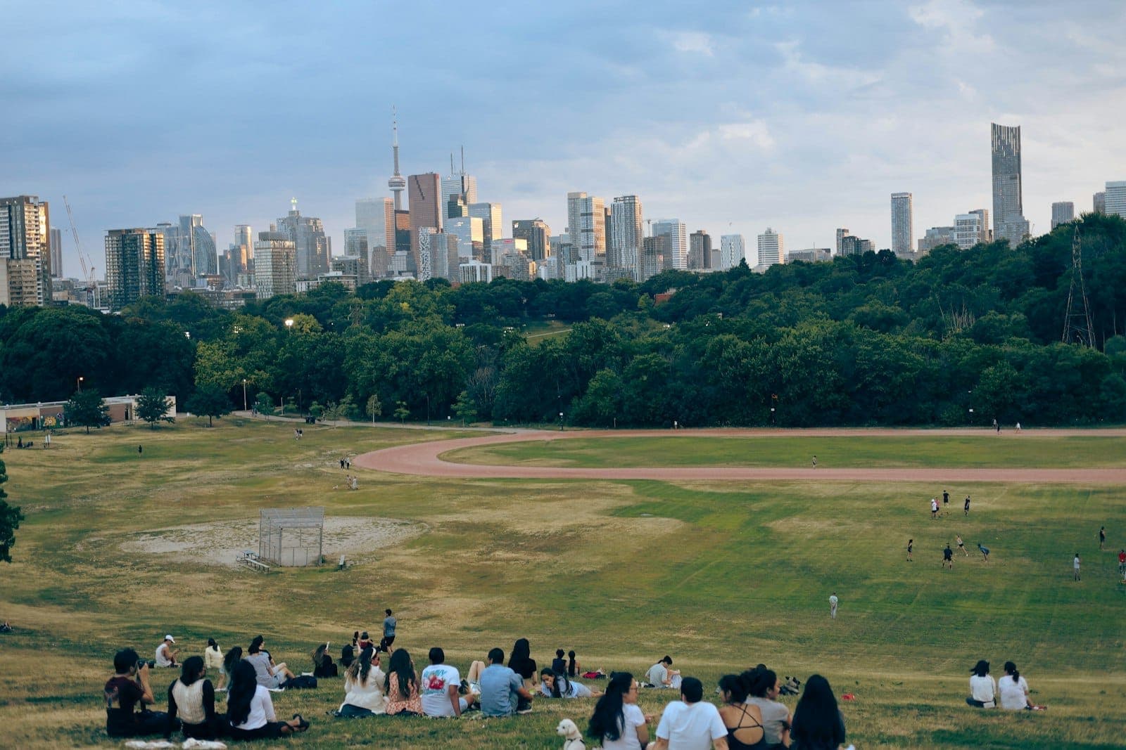 Vista del Riverdale Park East a Toronto, con persone che si rilassano sul pendio erboso e lo skyline del centro città sullo sfondo al tramonto.