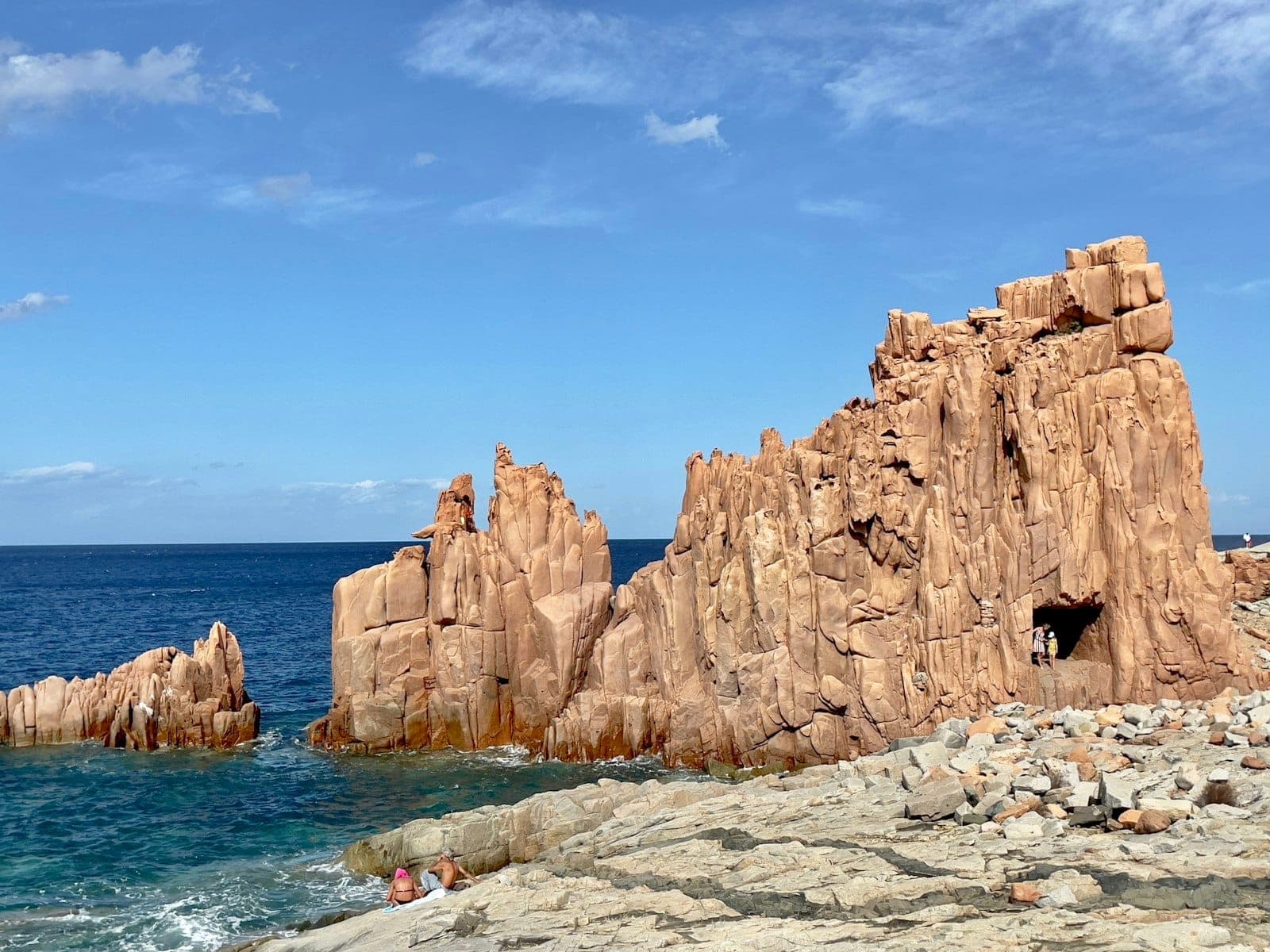 Los impresionantes acantilados de pórfido rojo de Rocce Rosse di Arbatax se elevan abruptamente sobre el azul Mar Tirreno bajo un cielo despejado y luminoso.