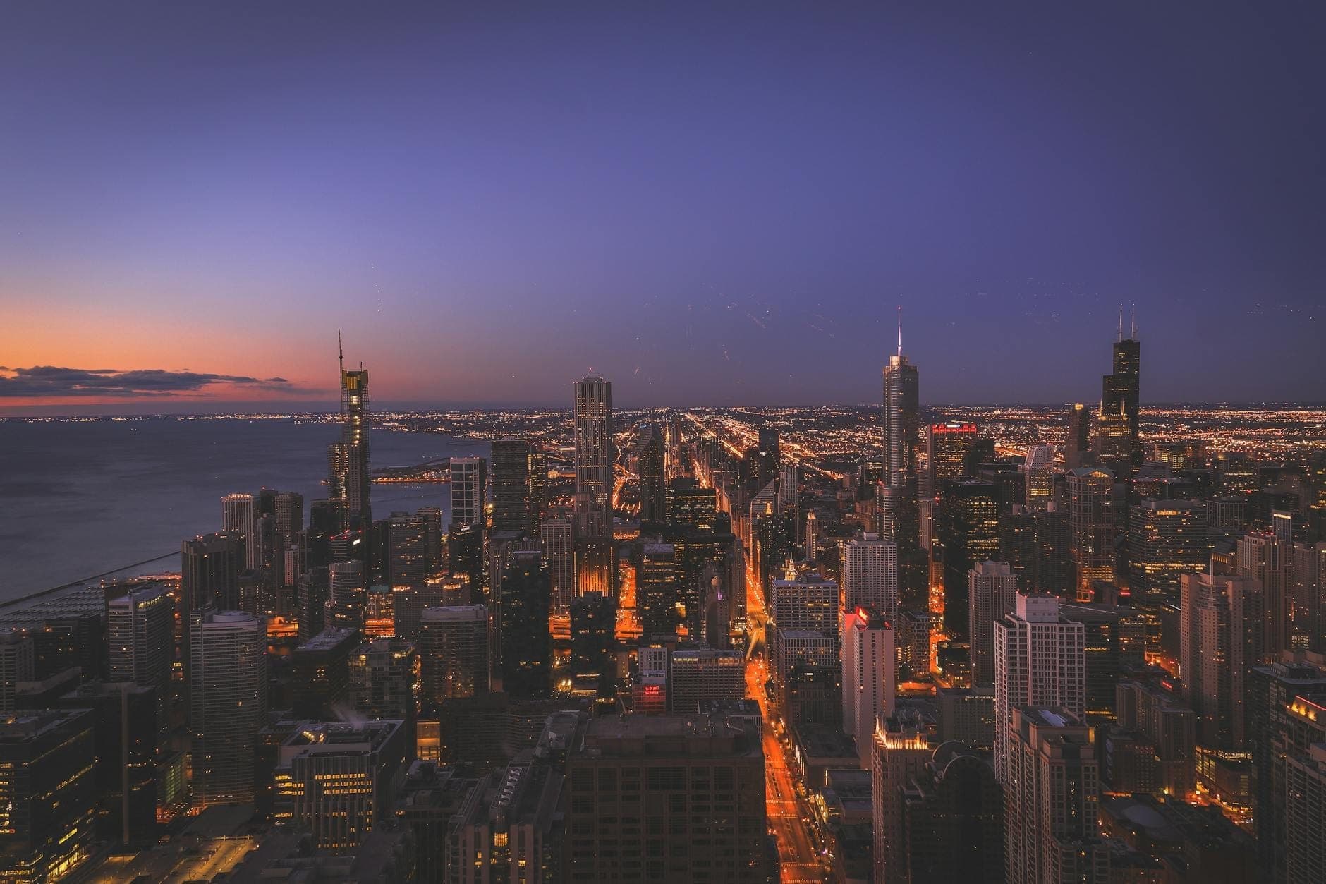 Chicago skyline at dusk with illuminated buildings and Lake Michigan, showcasing the city’s iconic high-rises and romantic twilight atmosphere.