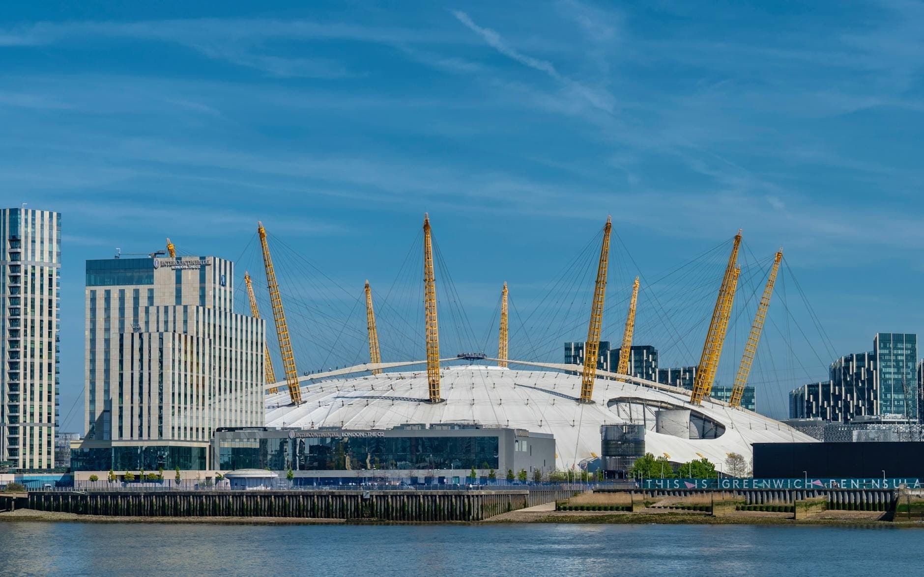 Vue de jour de l'O2 Arena à Londres avec des bâtiments modernes et la Tamise au premier plan.