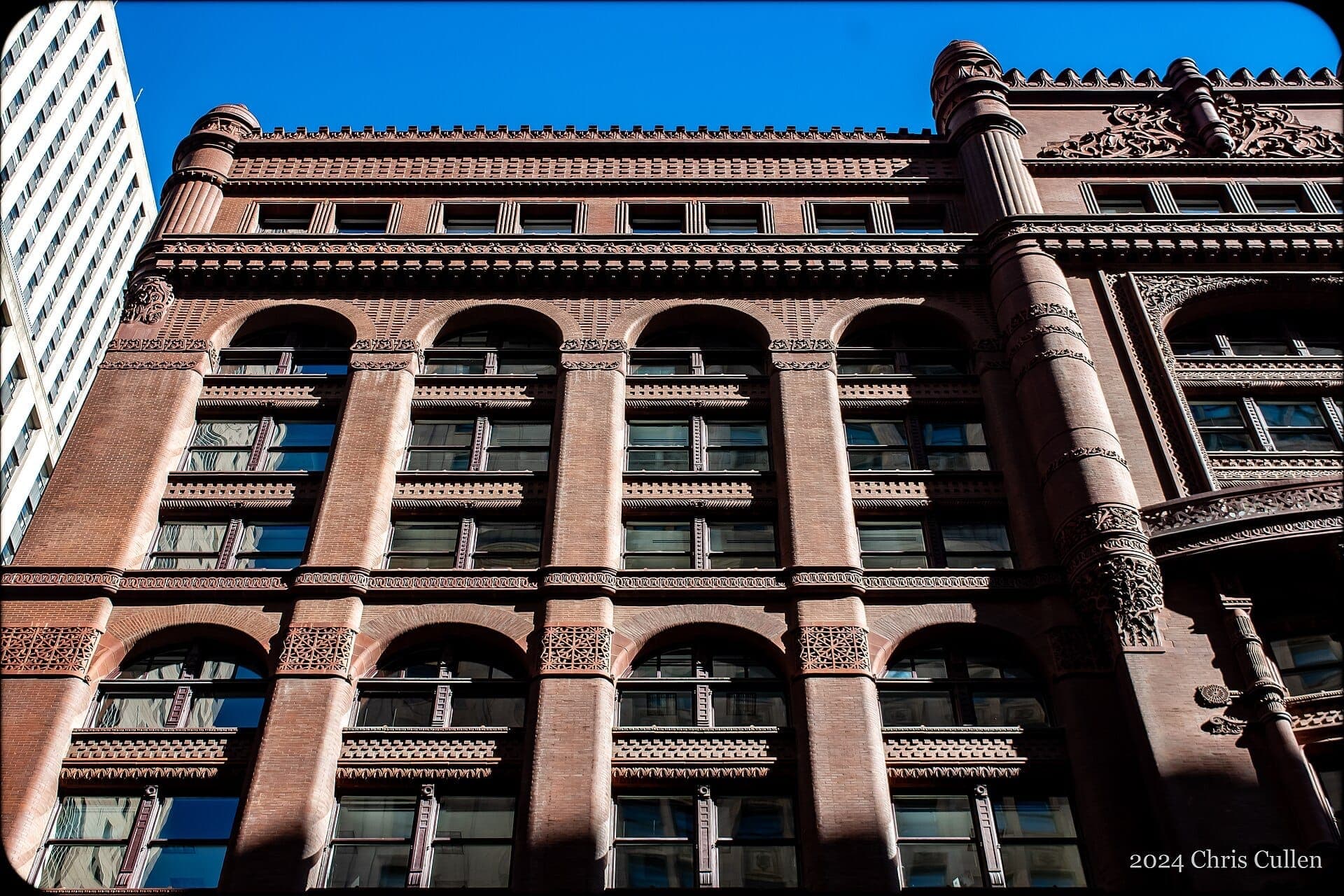 Detailed view of the Rookery Building’s historic red brick facade and ornate architectural elements against a clear blue Chicago sky.
