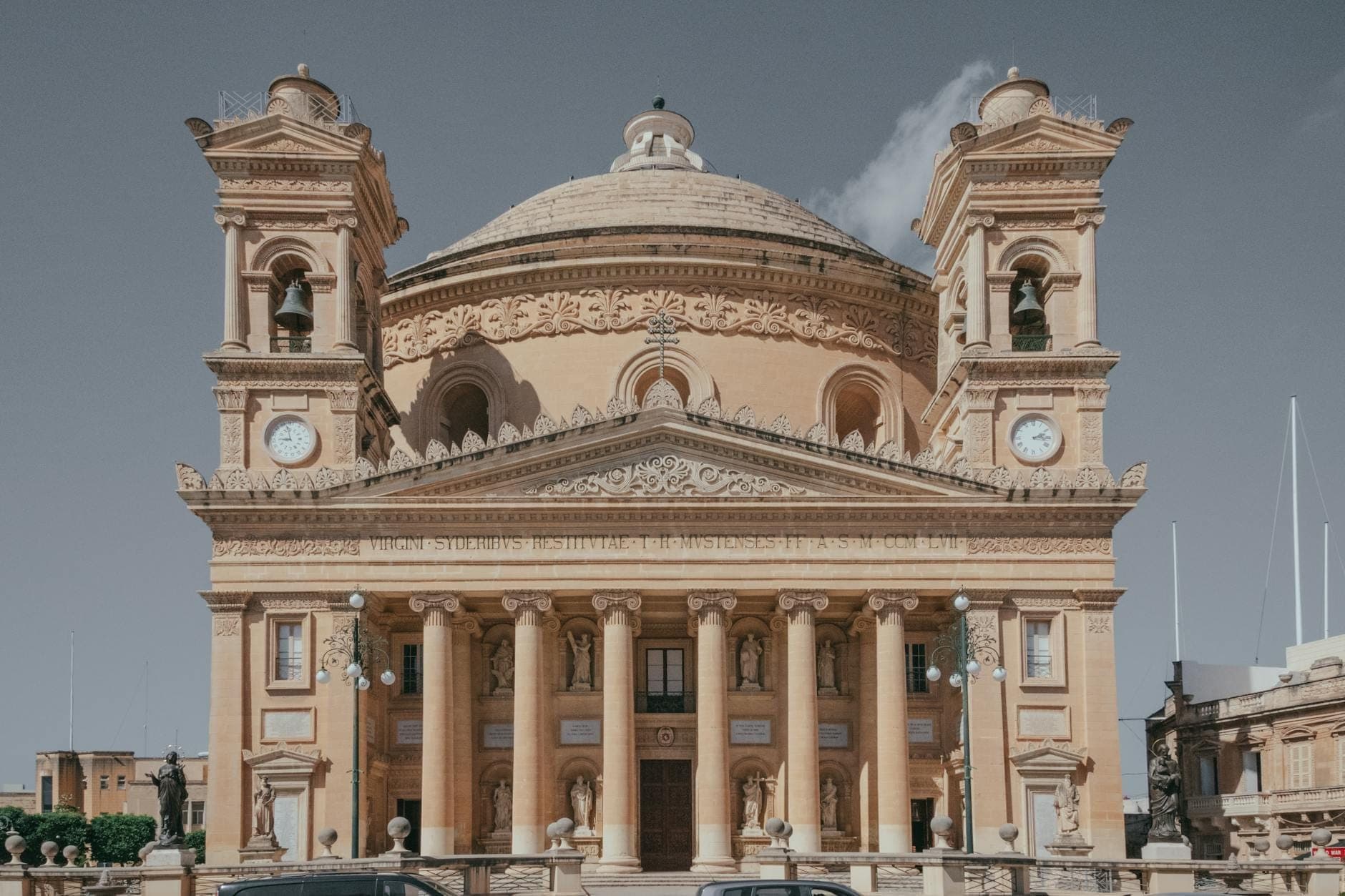 Frontansicht der Rotunde von Mosta mit ihrer imposanten neoklassizistischen Fassade, der großen Kuppel und zwei Glockentürmen unter klarem Himmel.