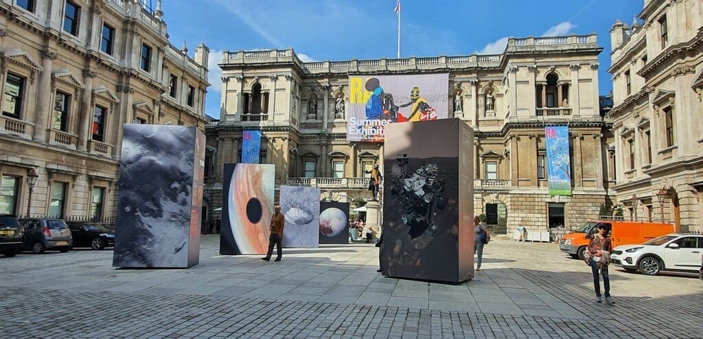 Der Innenhof der Royal Academy of Arts in London mit großen zeitgenössischen Kunstinstallationen und klassischer palladianischer Architektur unter einem strahlend blauen Himmel.