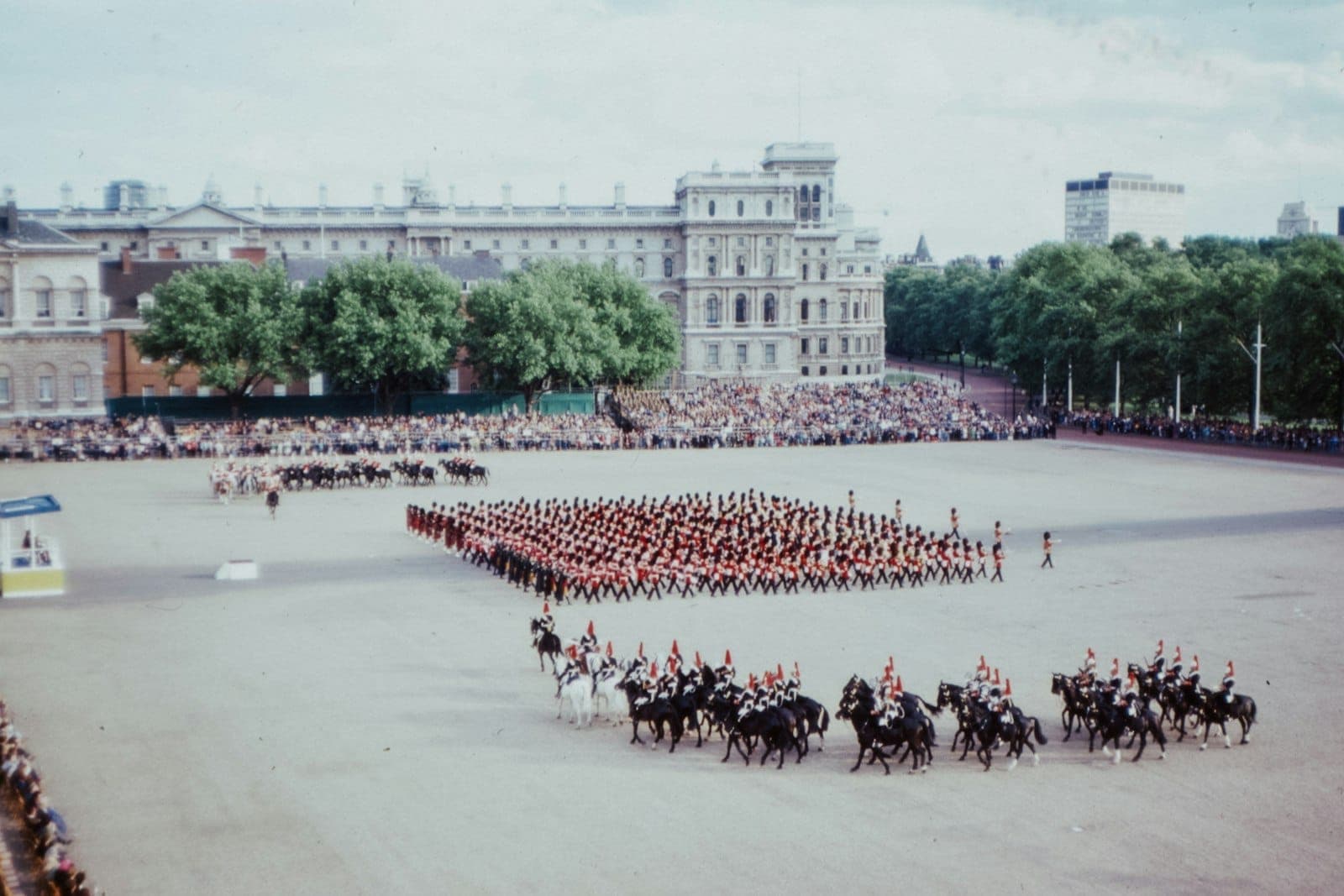 A grand royal parade with soldiers and horse guards in formation at Horse Guards Parade, London, watched by large crowds and historic buildings.