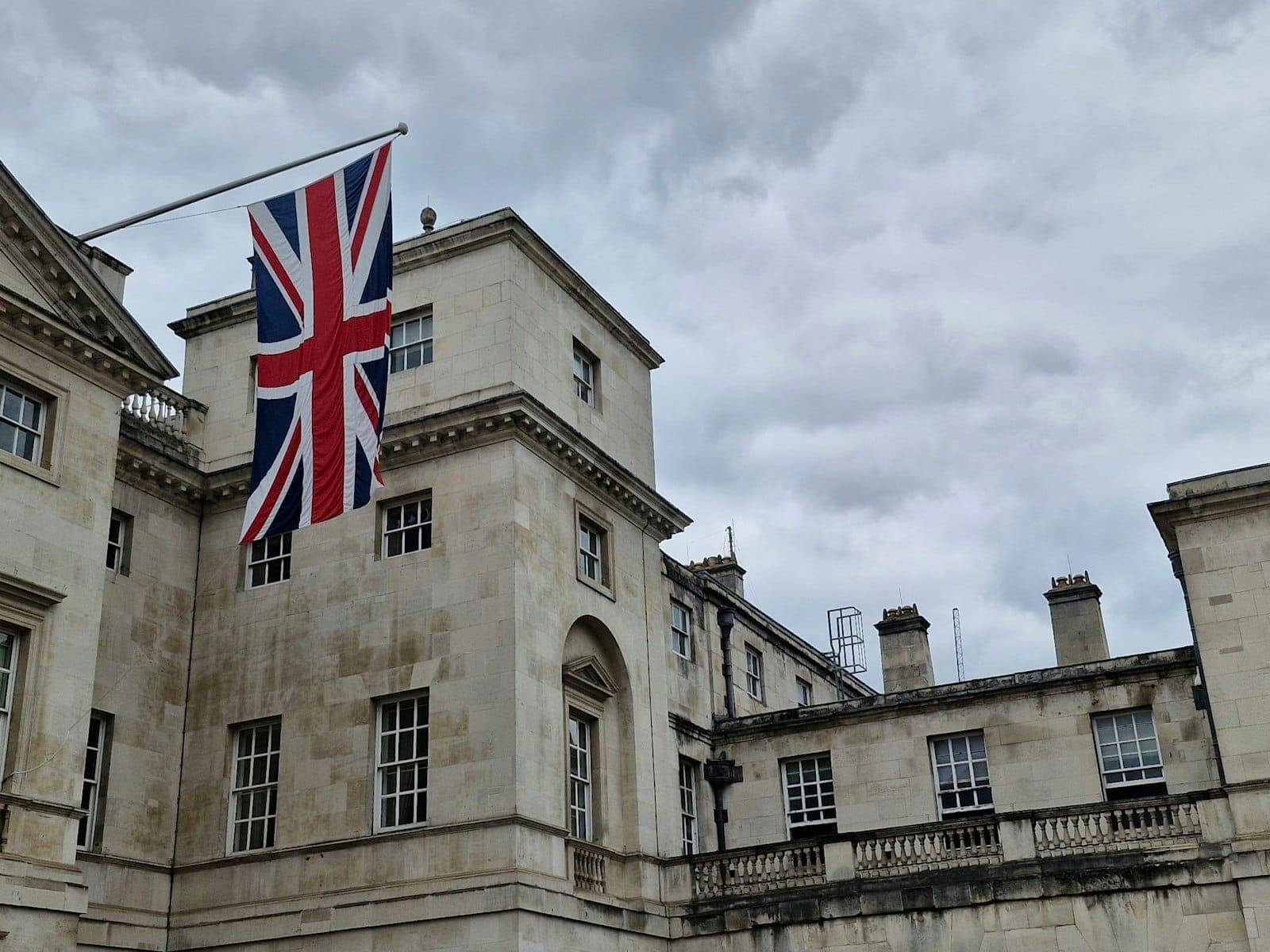 A grand stone building in London flying a large Union Jack flag, evoking British heritage and royal tradition.