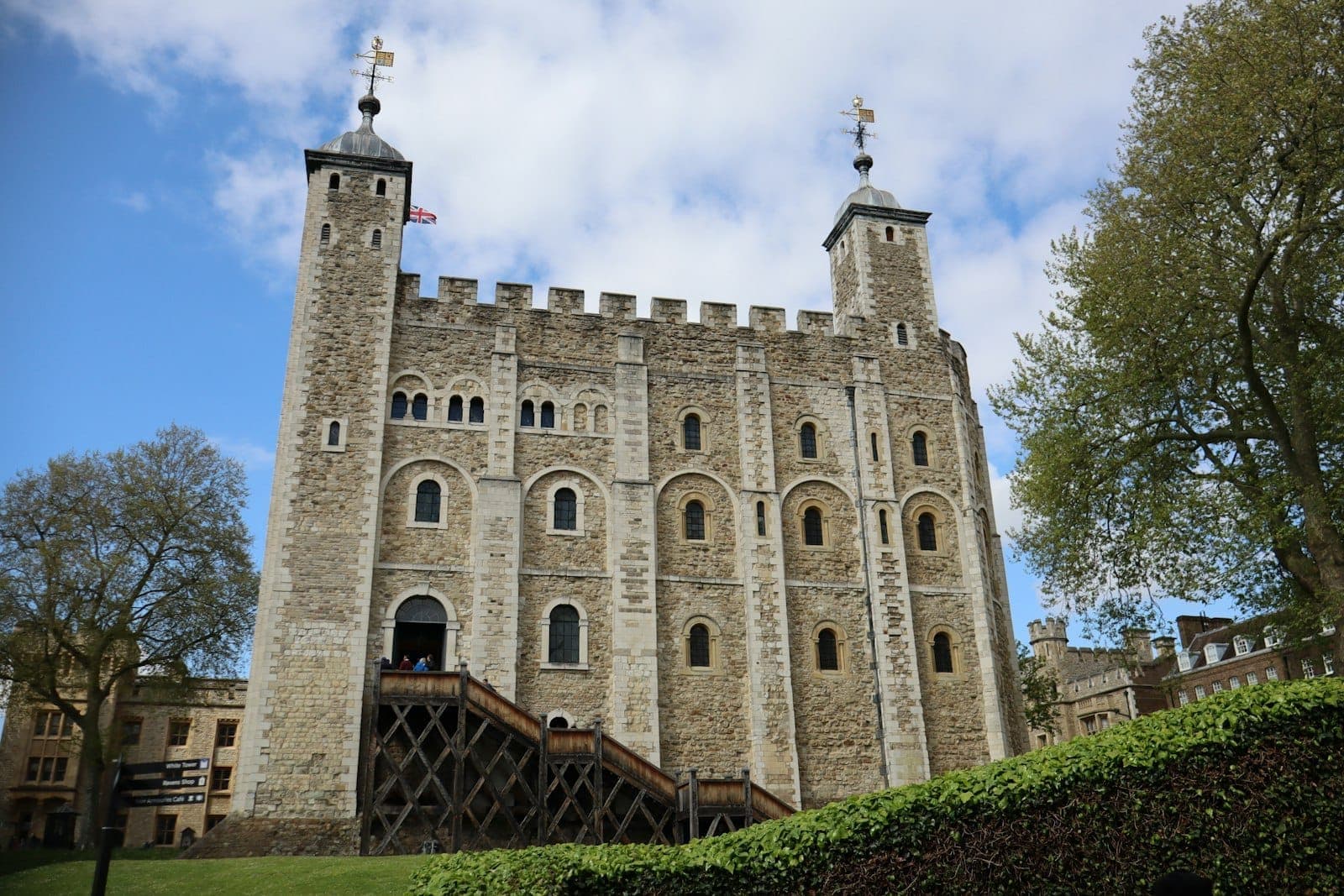 The White Tower at the Tower of London, a massive stone medieval fortress with twin turrets, seen on a bright day with blue sky and green grass.