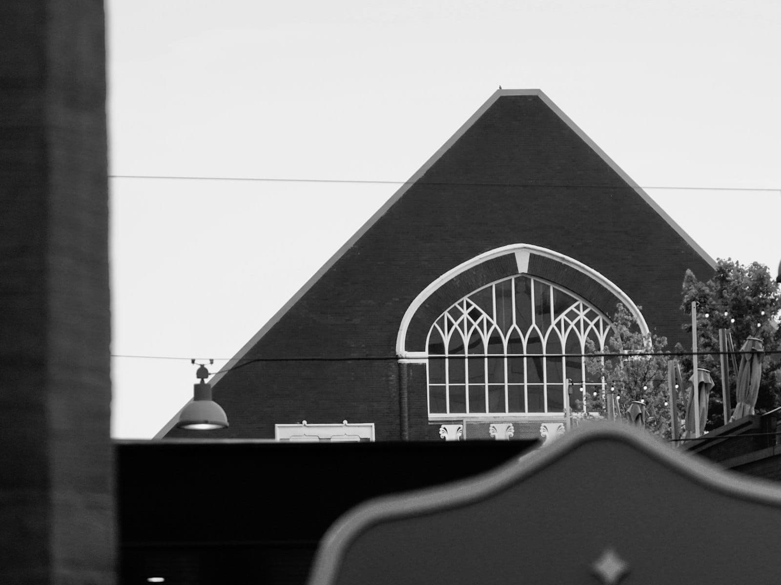 El distintivo techo triangular y la ventana de vitral con arco del exterior del Ryman Auditorium en blanco y negro, enmarcados contra un cielo luminoso.