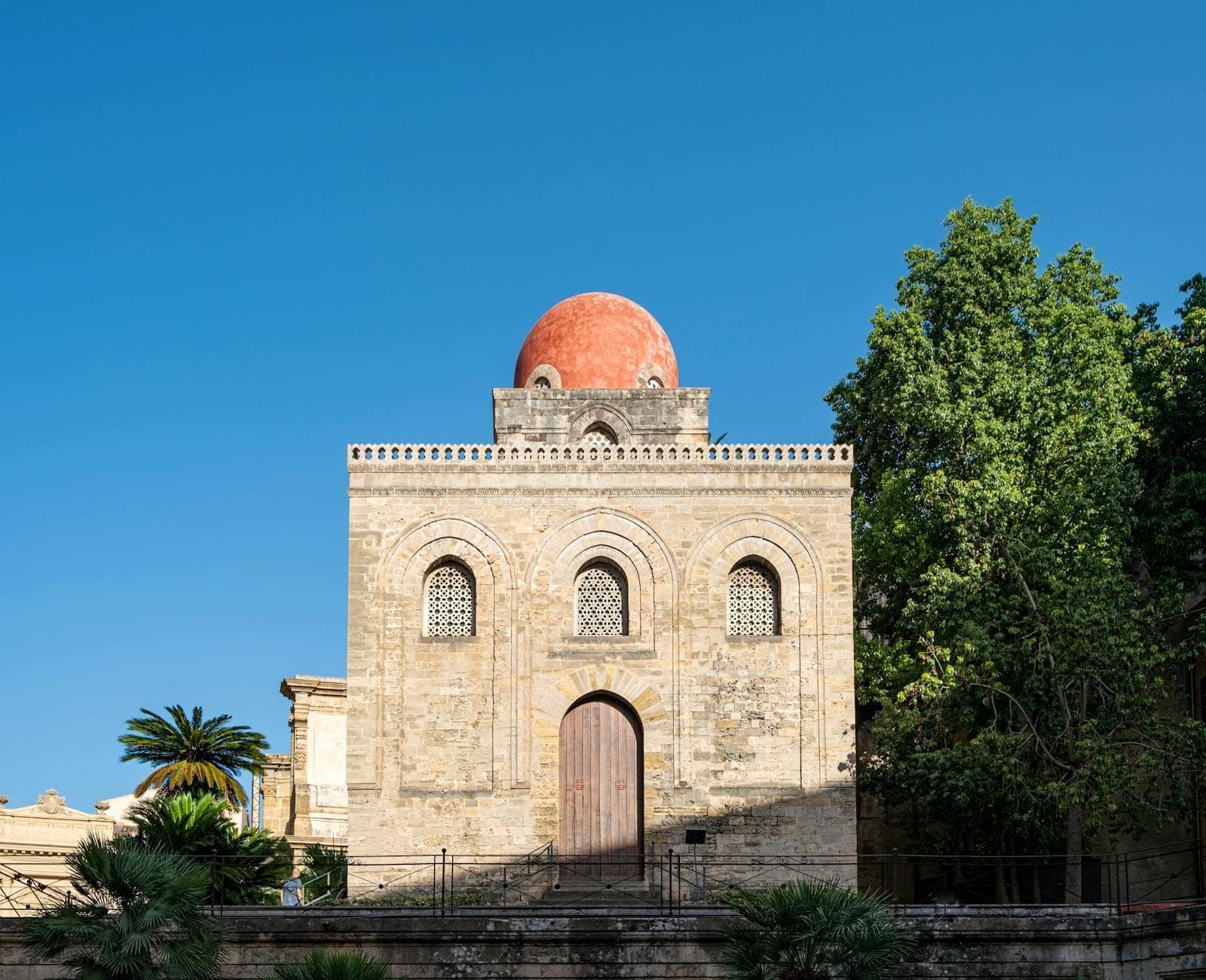 Tampak depan Gereja San Cataldo di Palermo, memperlihatkan fasad batu dan kubah merah khasnya di bawah langit biru cerah.