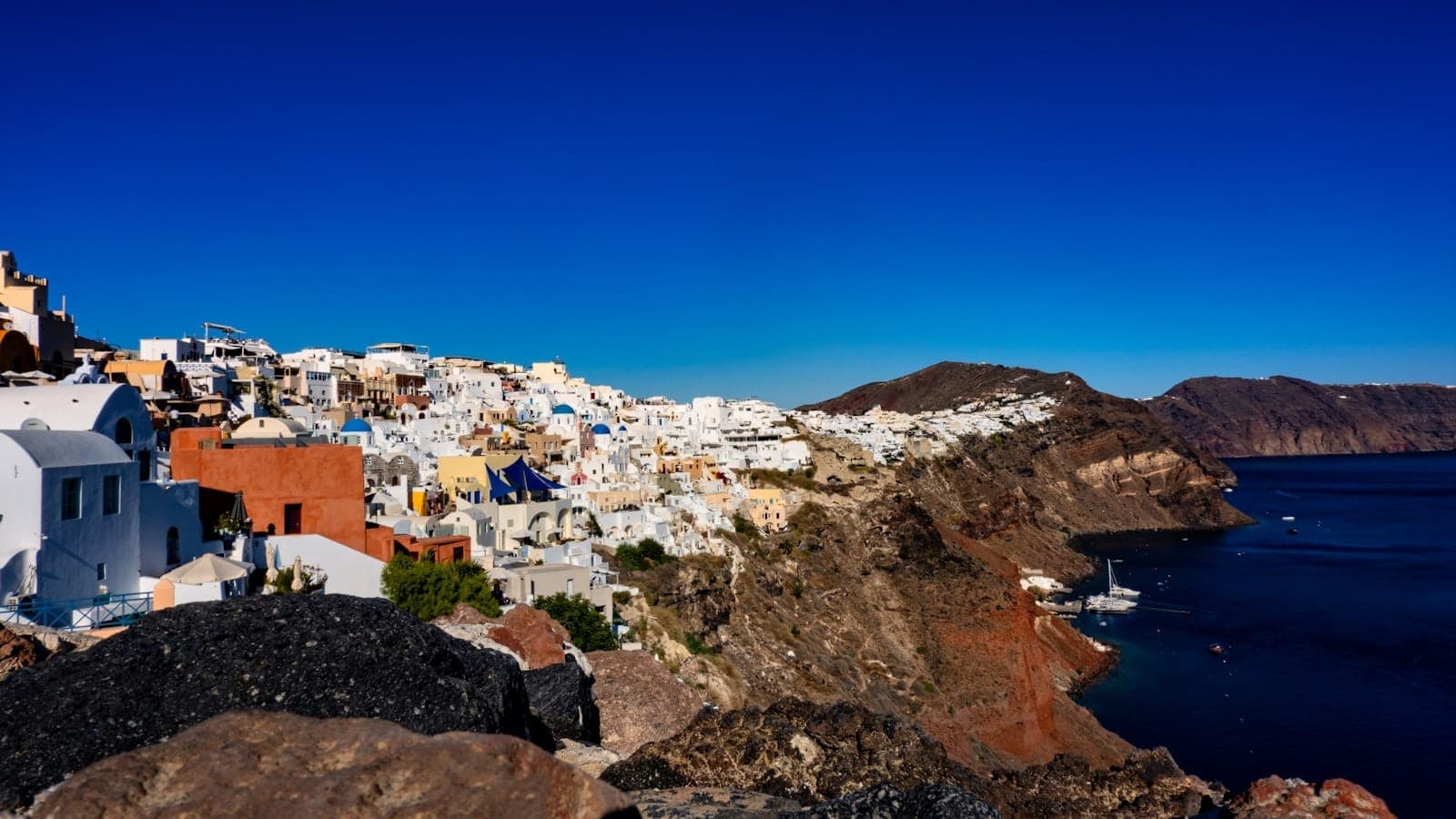 Blick auf Santorinis Klippendörfer mit weiß getünchten Häusern, Vulkangestein und tiefblauem Meer unter einem satten blauen Himmel – die dramatische und verborgene Landschaft der Insel.