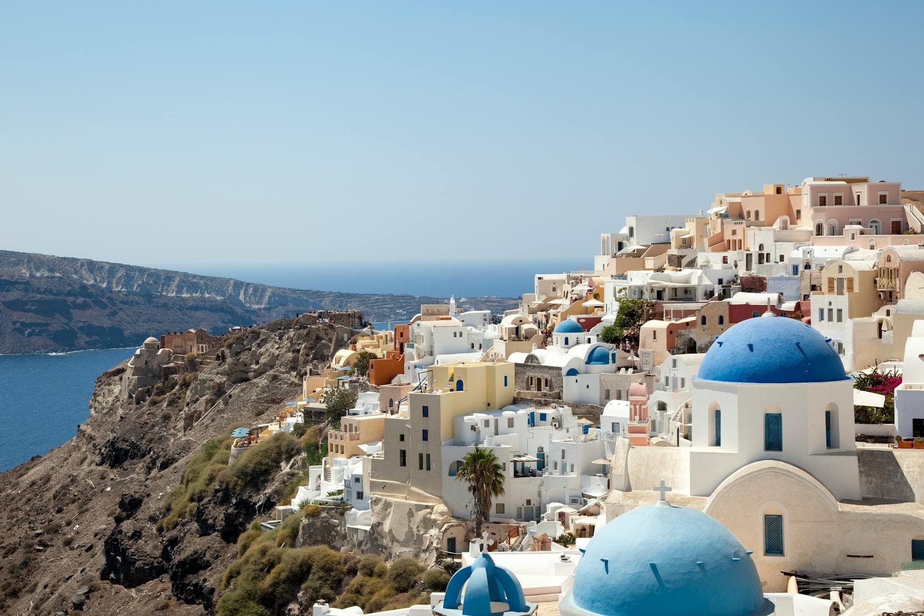 Vista classica di Santorini con chiese a cupola blu, edifici imbiancati e spettacolari scogliere della caldera che si affacciano sul mare blu profondo.