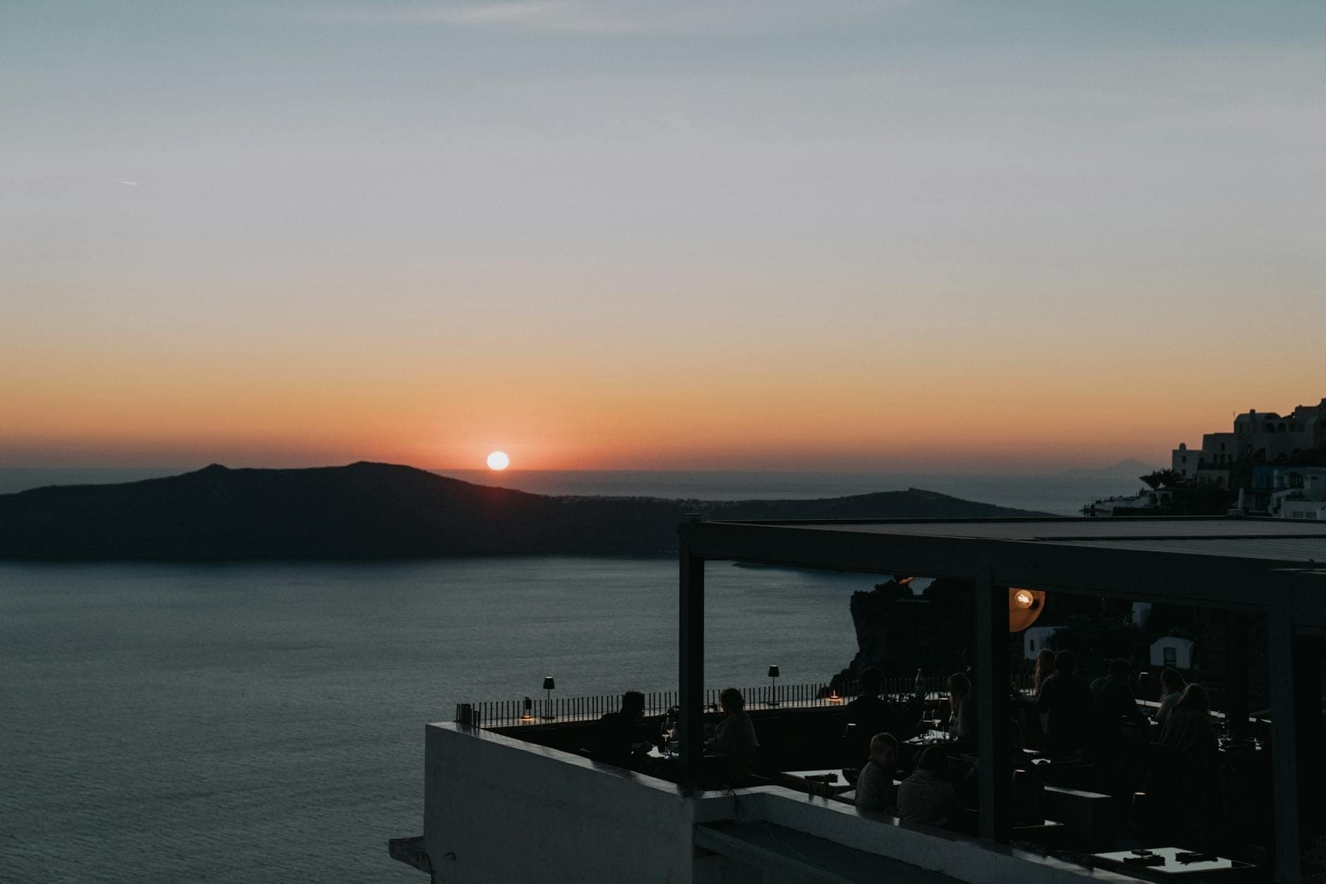 Vista al tramonto da un ristorante sul tetto con commensali che si affacciano sulla caldera di Santorini e sul mare.
