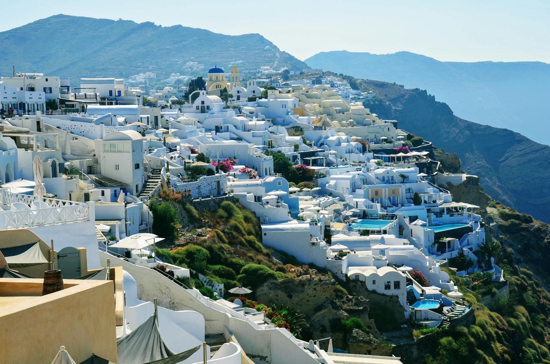Ampia vista degli iconici hotel e ville intonacati di bianco di Santorini sul dirupo con vista sulla caldera, con piscine e terrazze, ideale per un soggiorno di luna di miele.