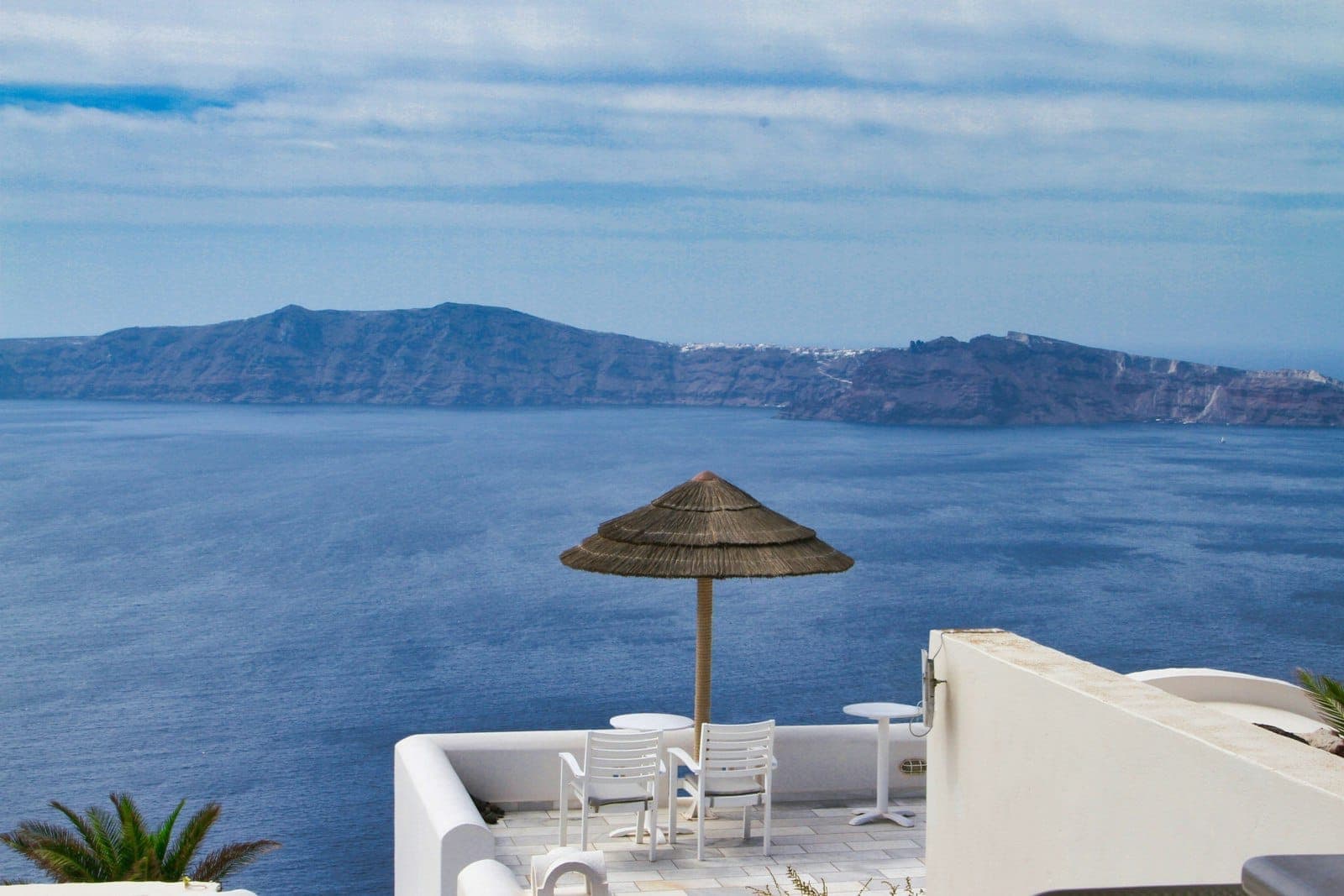 Terraza con vistas a la caldera con tumbonas y sombrilla frente a los acantilados volcánicos de Santorini y el azul mar Egeo.