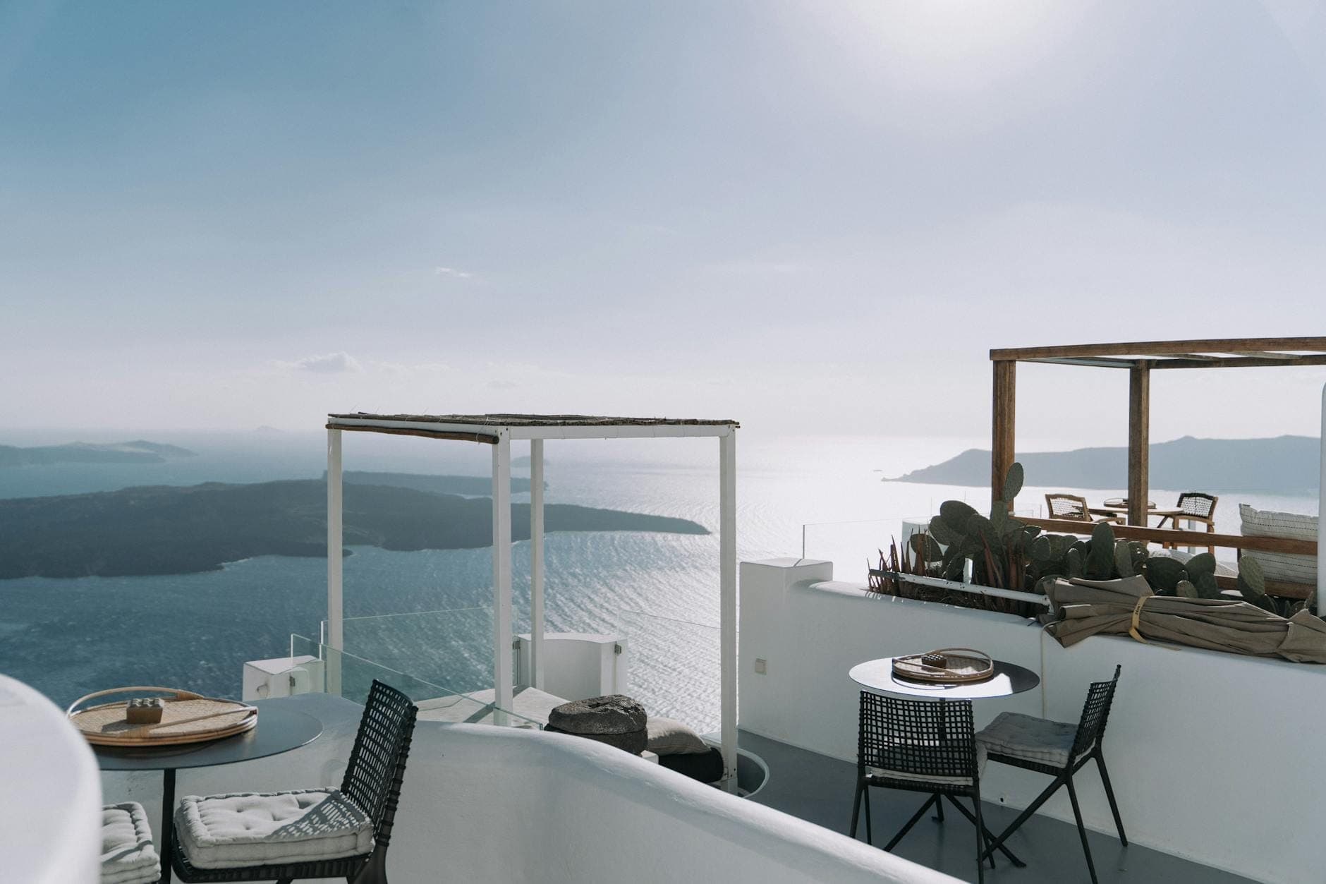 Luxuriöse Klippentetrasse mit eleganten Outdoormöbeln und Blick auf das blaue Meer und die Caldera Santorins im Sonnenuntergang – Entspannung auf höchstem Niveau.