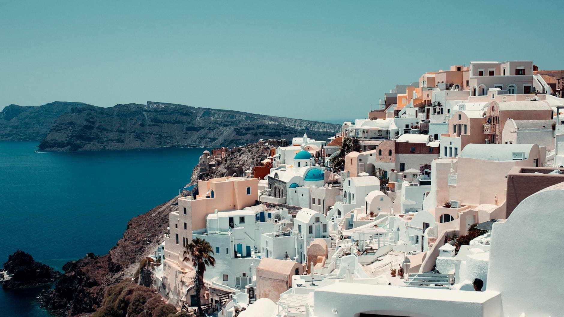 Daytime view of Santorini’s iconic white-washed houses and blue-domed churches perched on cliffs overlooking the sparkling blue sea.