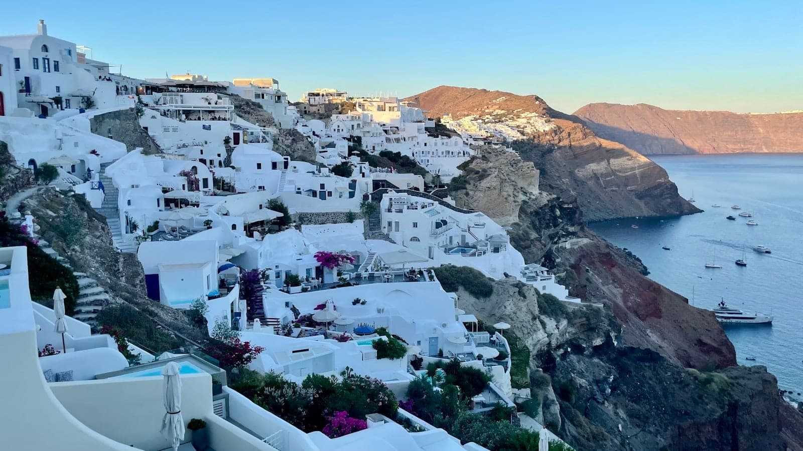View of Santorini’s whitewashed cliffside buildings overlooking the blue sea with clear sky, early morning sunlight, and minimal crowds.