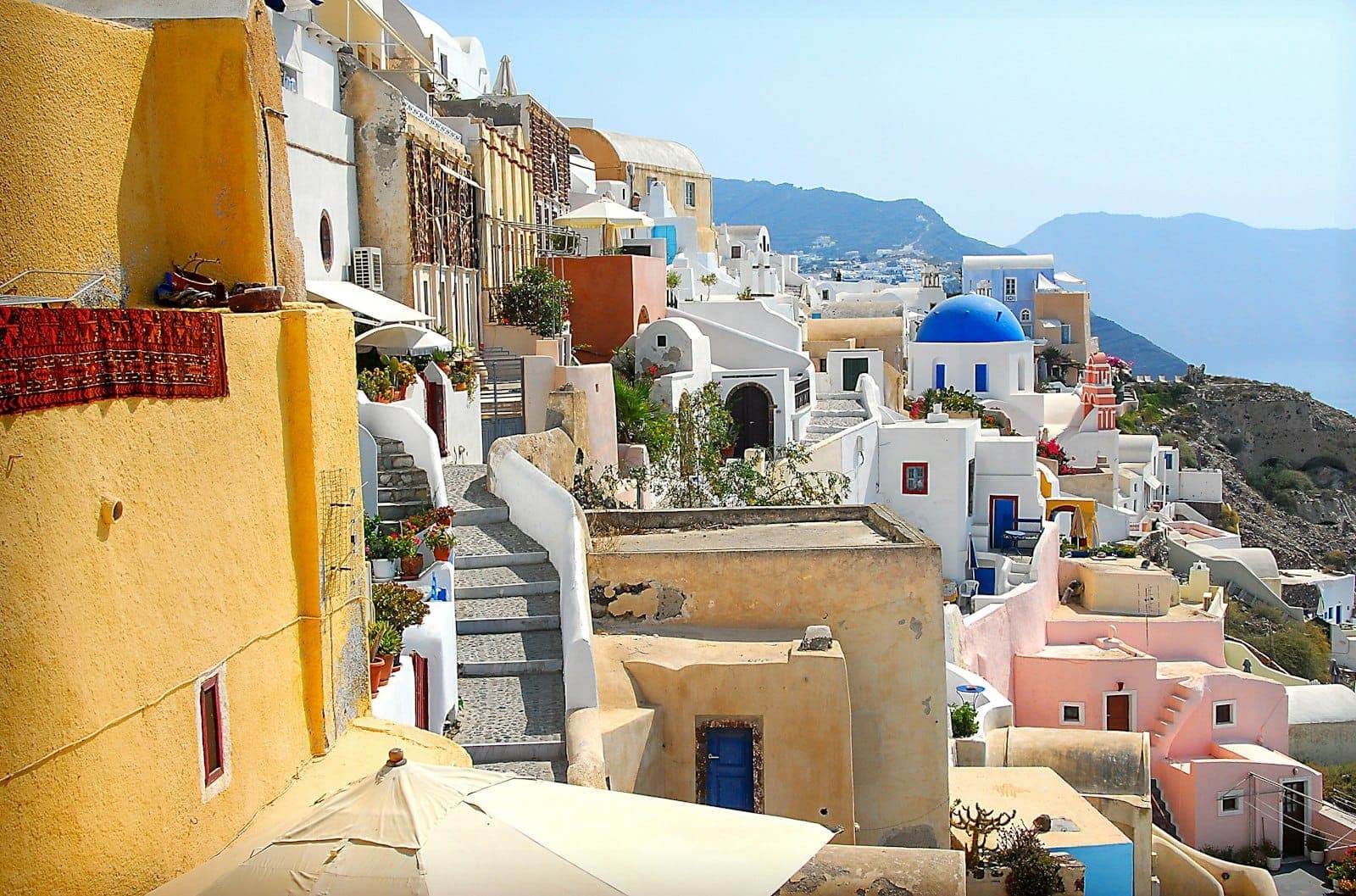 Dorfszene in Santorini mit bunten Häusern, blaukuppligen Kirchen, engen Gassen und traditioneller kykladischer Architektur unter klarem Himmel.