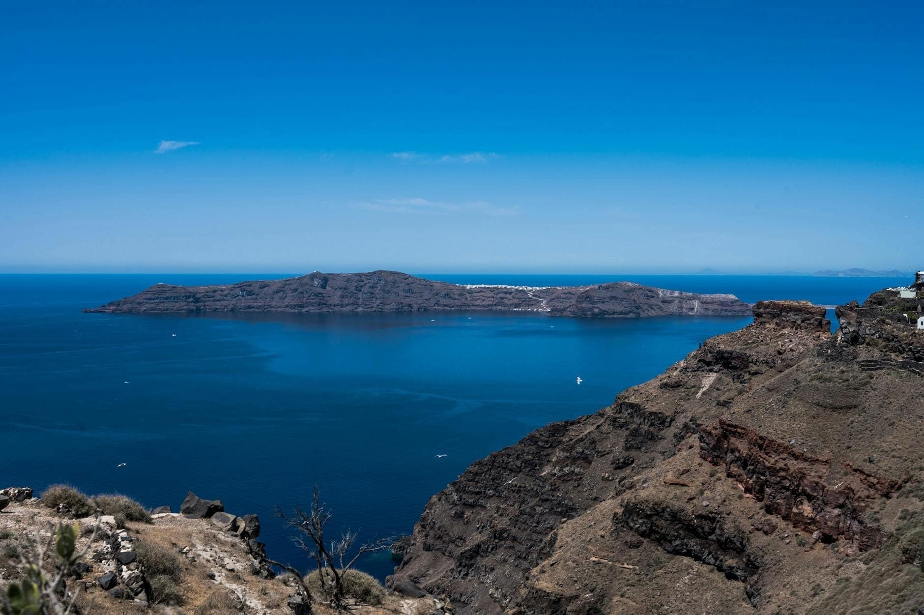 Vulkanische Klippen und felsige Küste von Santorini mit blauem Meer und Caldera-Insel unter klarem Himmel