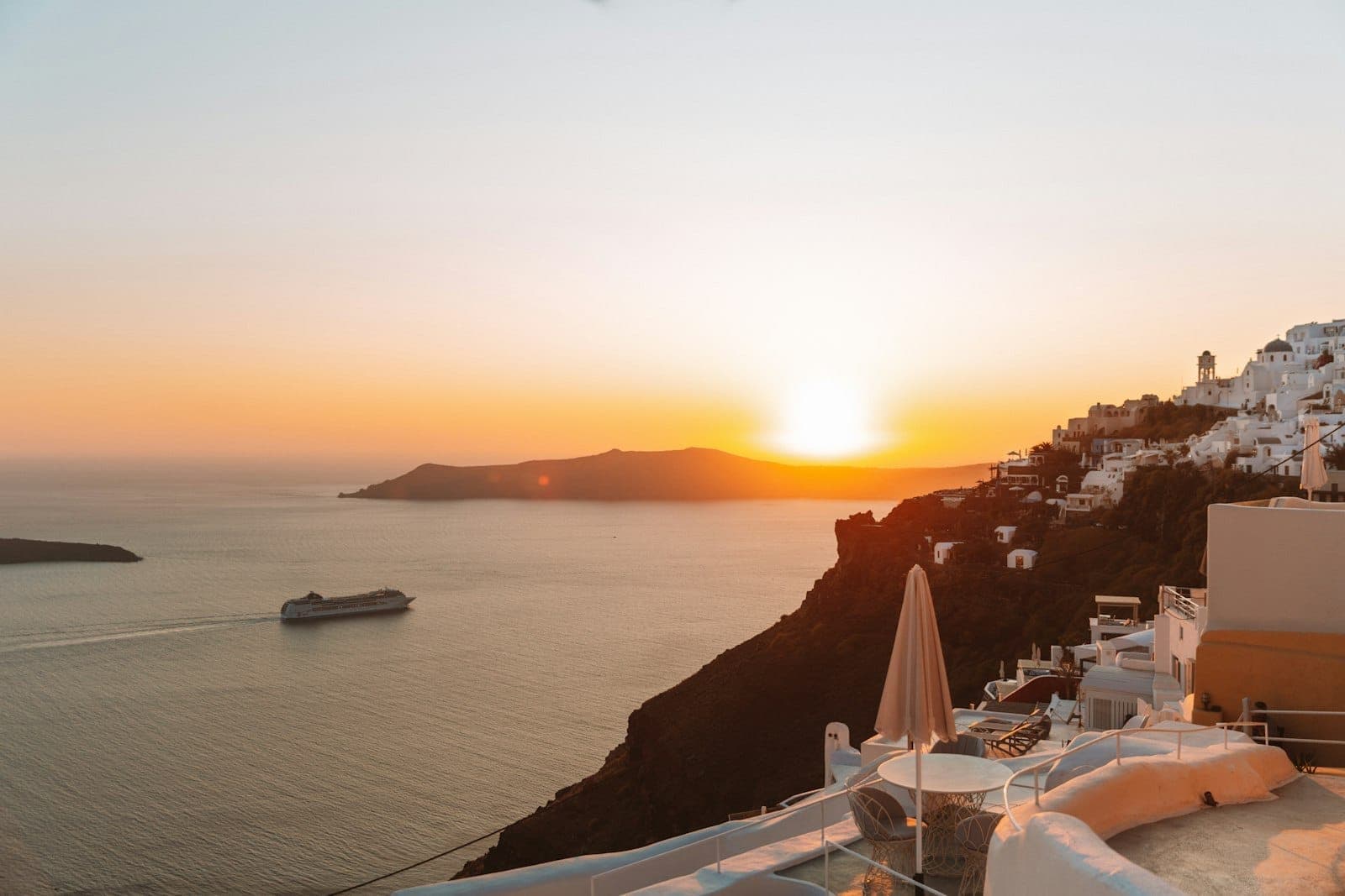 Goldener Sonnenuntergang über Santorini mit ruhigen weiß getünchten Terrassen und einem Kreuzfahrtschiff in der Caldera, der ein ruhiges und außergewöhnliches Abendlicht heraufbeschwört.
