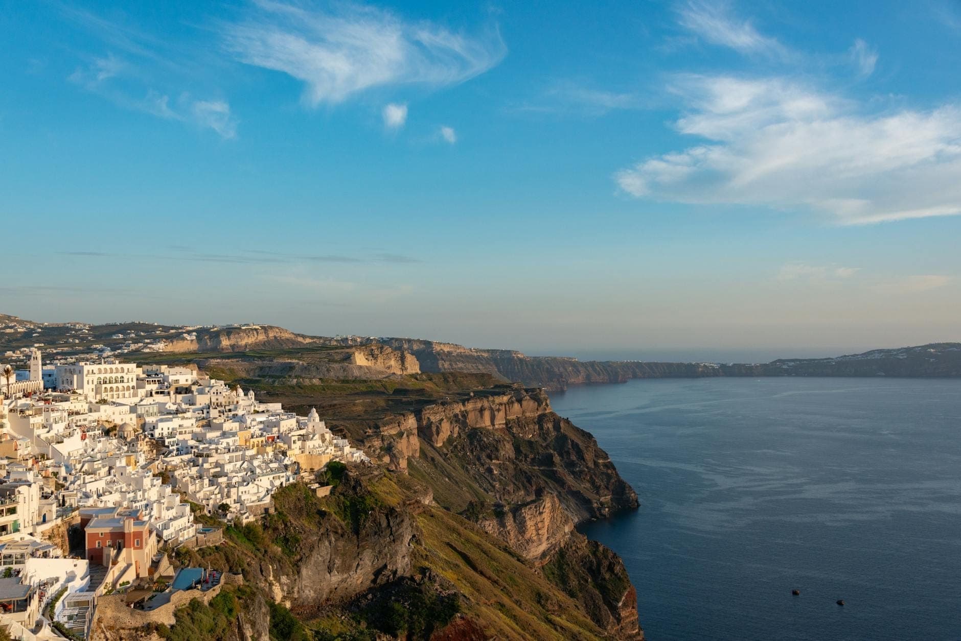Blick auf den Rand der Santorini-Caldera mit weißen Gebäuden auf dramatischen Klippen mit Blick auf das Ägäische Meer unter blauem Himmel.