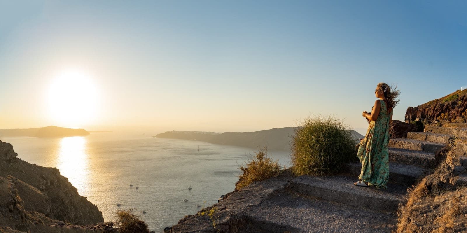 Frau auf einem Weg mit Blick auf die Santorini-Caldera bei Sonnenuntergang, mit weitem Panorama und goldenem Abendlicht