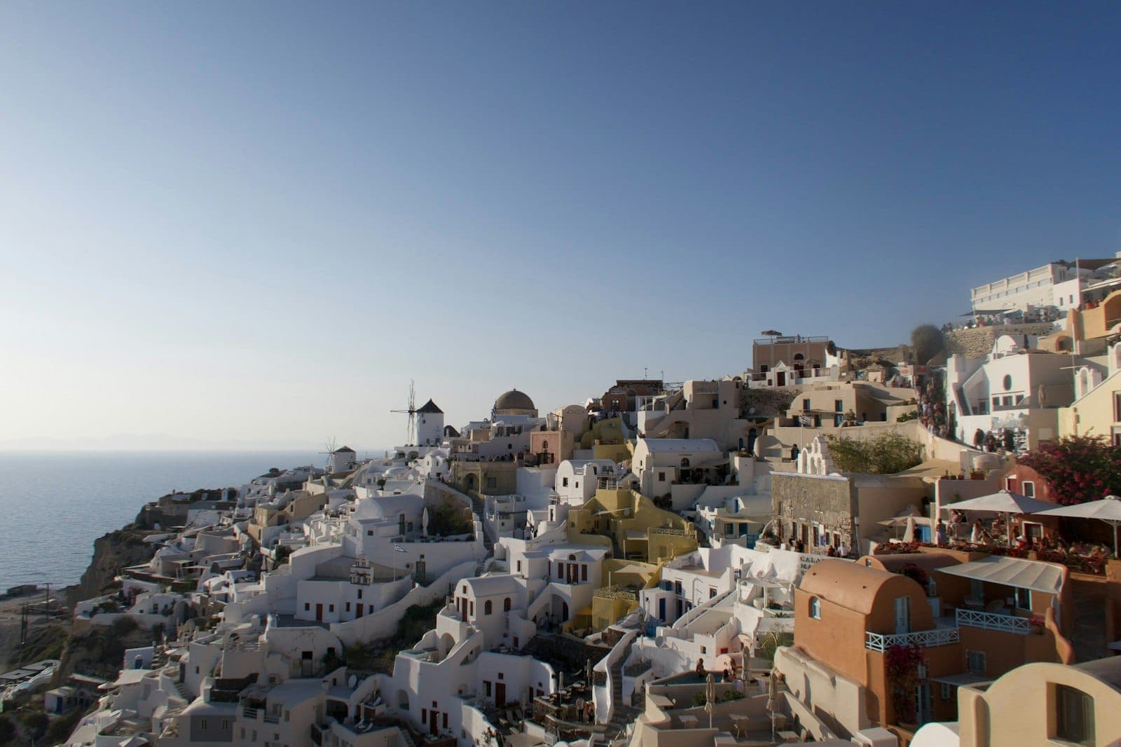 Vista panorámica de las icónicas casas encaladas y cúpulas azules de Santorini en un día soleado, con cielos despejados y el mar visible al fondo.