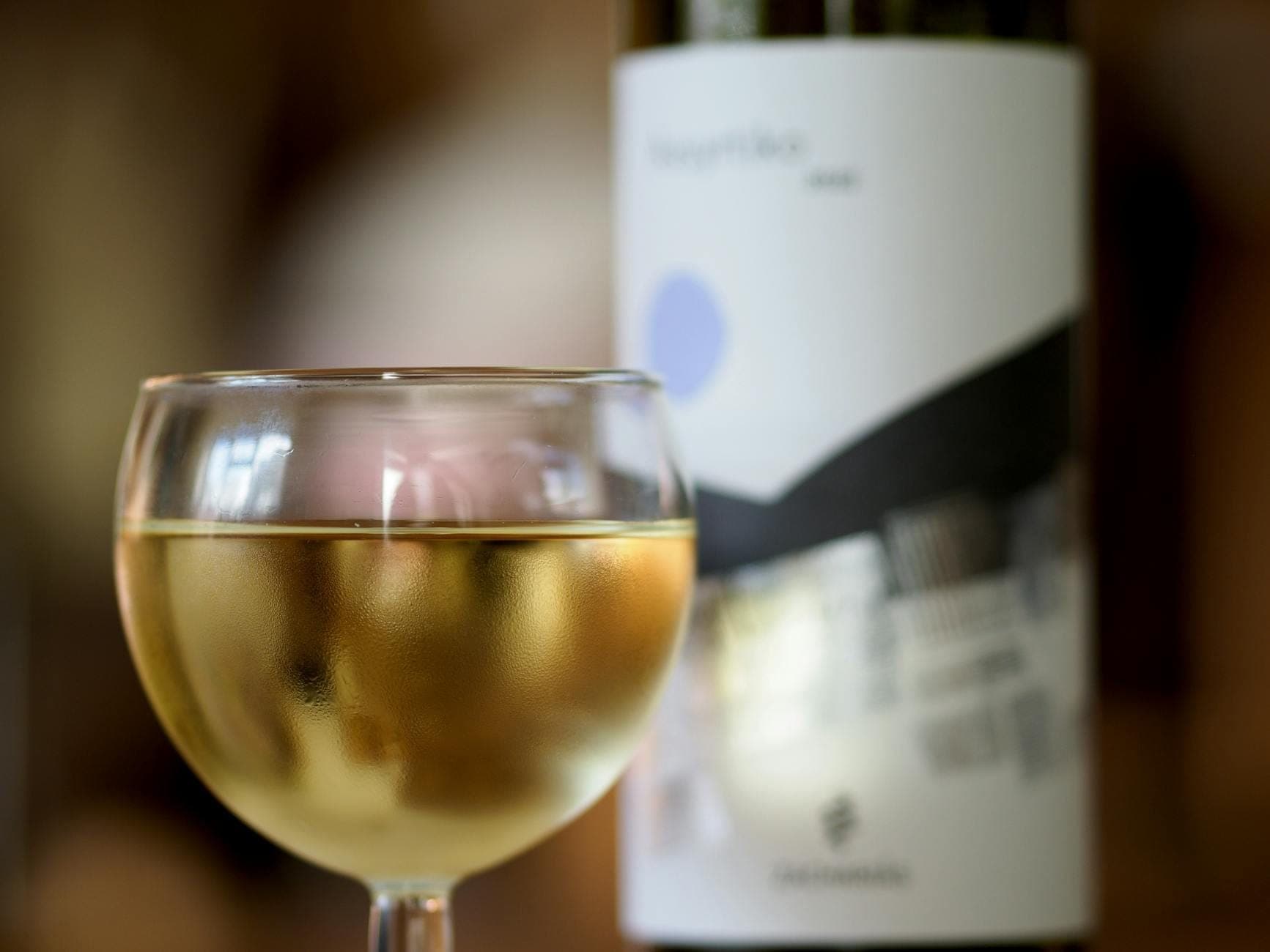 Nahaufnahme eines Glases Weißwein mit einer Flasche im Hintergrund – Atmosphäre einer griechischen Weinverkostung.