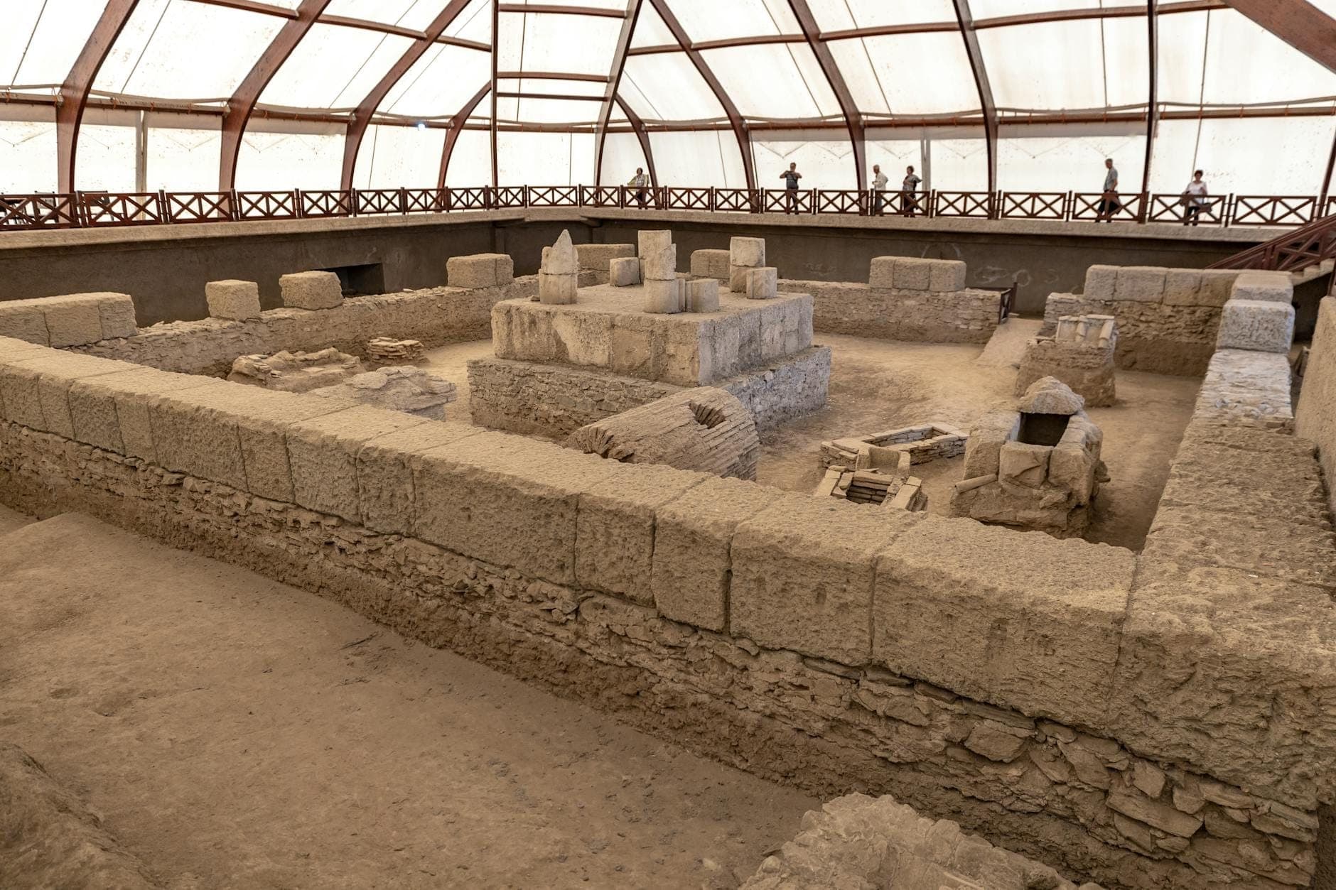 Vista interior del sitio arqueológico de Akrotiri en Santorini bajo un techo moderno, con antiguas ruinas de piedra y pasarelas.