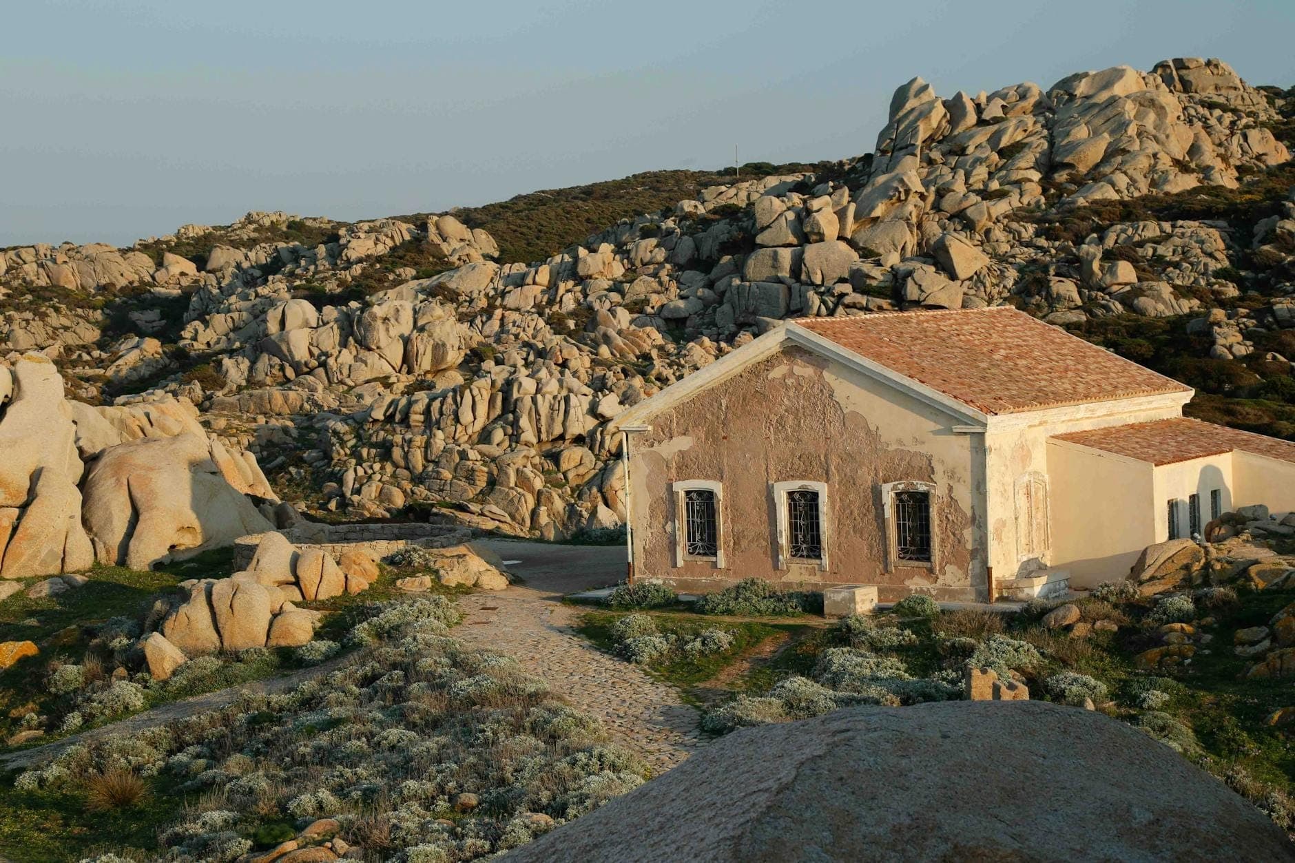 Casa de campo rústica con tejado de tejas entre rocas de granito en el interior de Cerdeña, bañada por la cálida luz del atardecer.