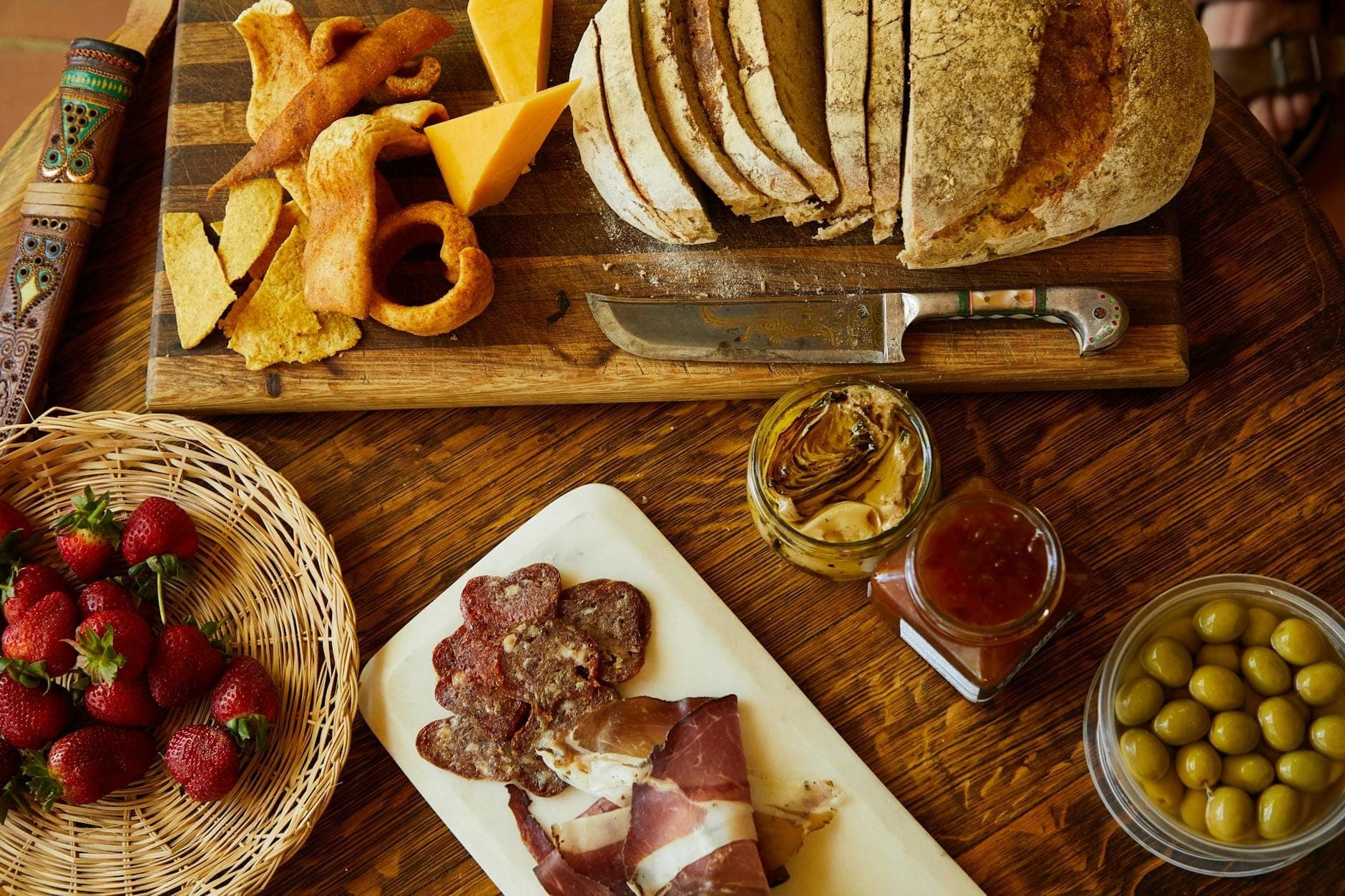 Una mesa rústica con pan en rebanadas, queso, embutidos, aceitunas, fresas y conservas, que refleja una comida típica sarda en la Zona Azul.