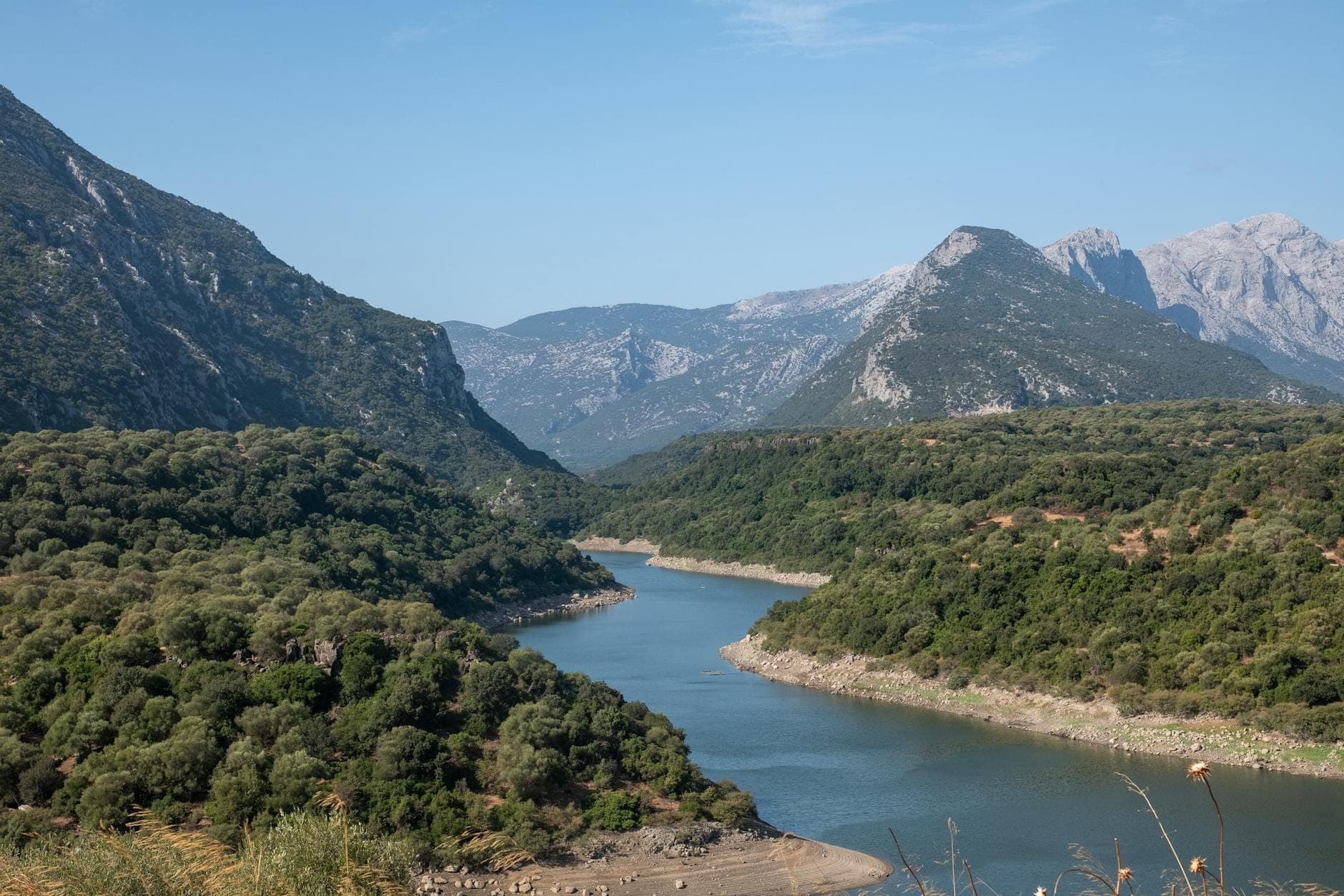 Vista panorámica de un río serpenteando entre colinas verdes y montañas en Cerdeña en un día despejado
