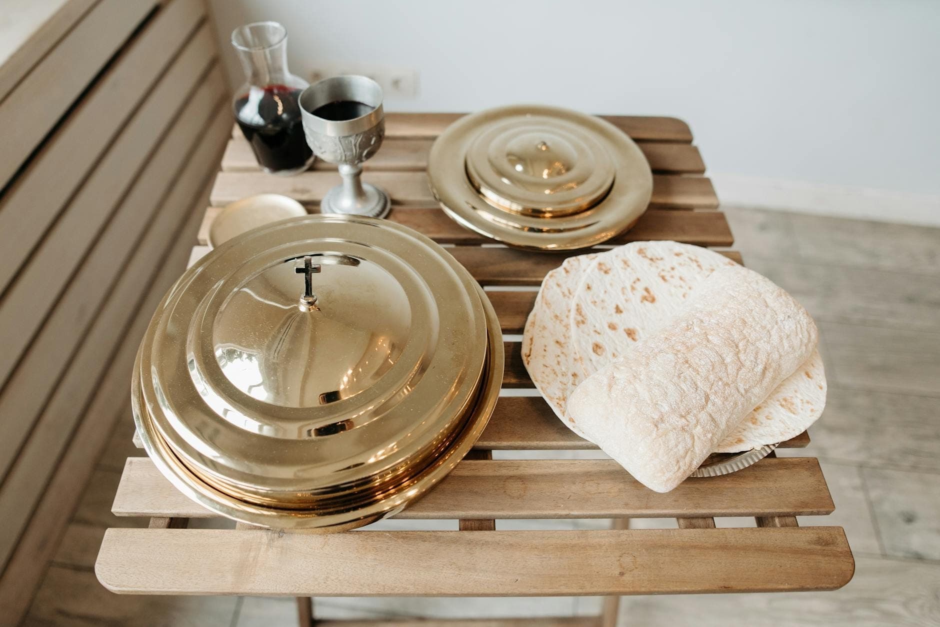 Una mesa de madera rústica con panes planos finos y redondos que recuerdan al pane carasau, junto a elegantes platos de servir de metal y una copa de vino tinto.