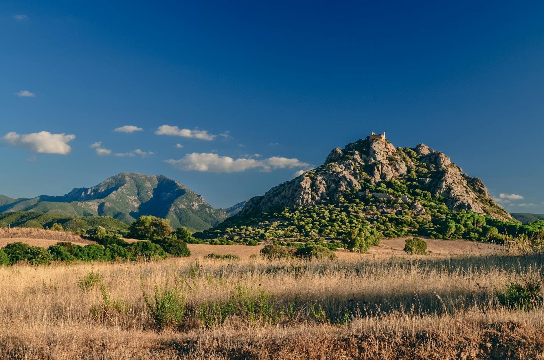 Cima rocosa en un paisaje rural de Cerdeña con ruinas antiguas visibles en lo alto del pico bajo un cielo azul.