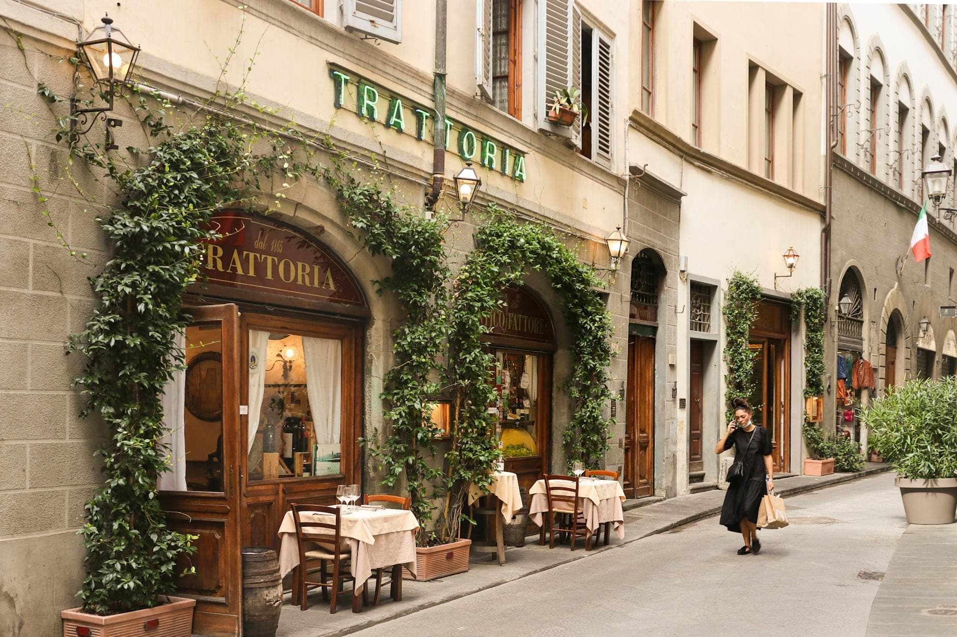 Encantadora trattoria con mesas al aire libre en una calle estrecha, con vegetación acogedora alrededor de la entrada, típica de los restaurantes locales económicos en Italia.