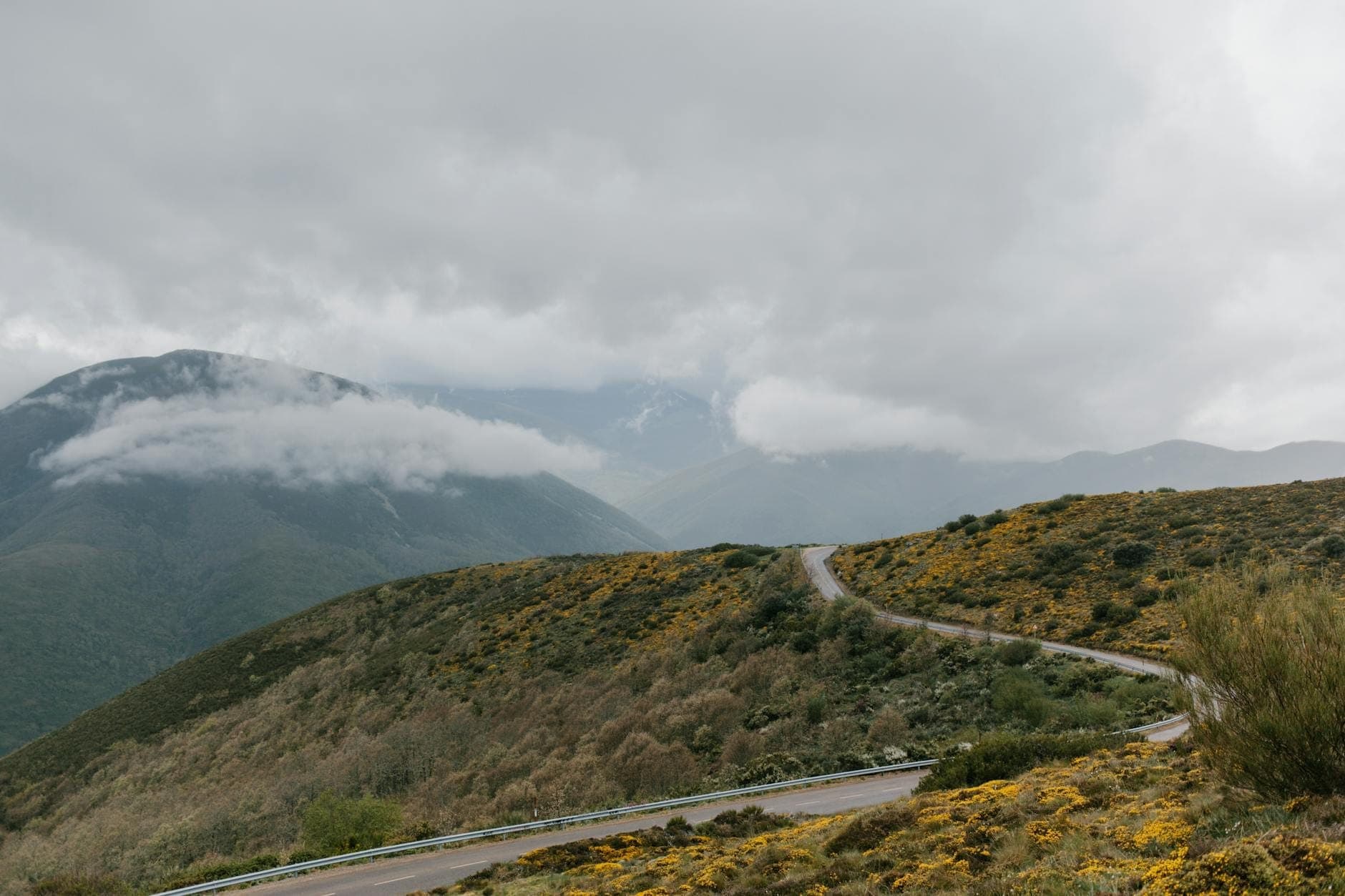 Kurvenreiche Bergstraße auf Sardinien mit dramatischen Hügeln und Wolken, die die Gipfel bedecken, ideal für einen malerischen Roadtrip.