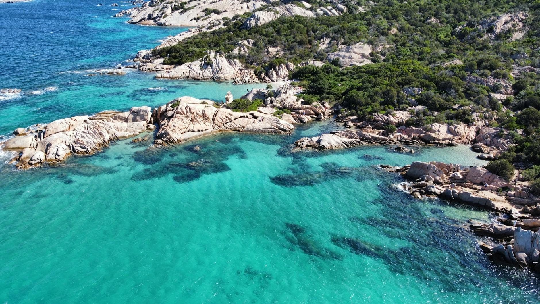 Luftaufnahme von türkisfarbenem Wasser und Granitfelsküste mit üppigem Grün, typisch für die malerischen Strände Nordsardiniens.