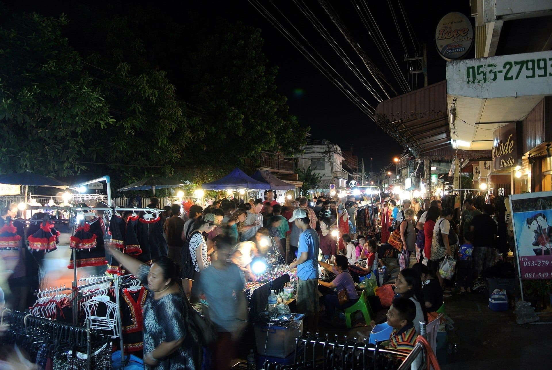 Menschenmengen versammeln sich unter den Marktlichtern der Saturday Walking Street in Chiang Mai auf der Wua Lai Road und stöbern nachts zwischen bunten Ständen und traditioneller Kleidung.
