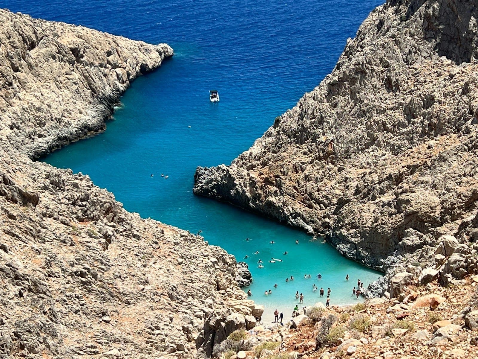 Luftaufnahme der Bucht Seitan Limani mit türkisfarbenem Wasser, steilen Felsklippen und Menschen, die an dem kleinen Sandstrand schwimmen.
