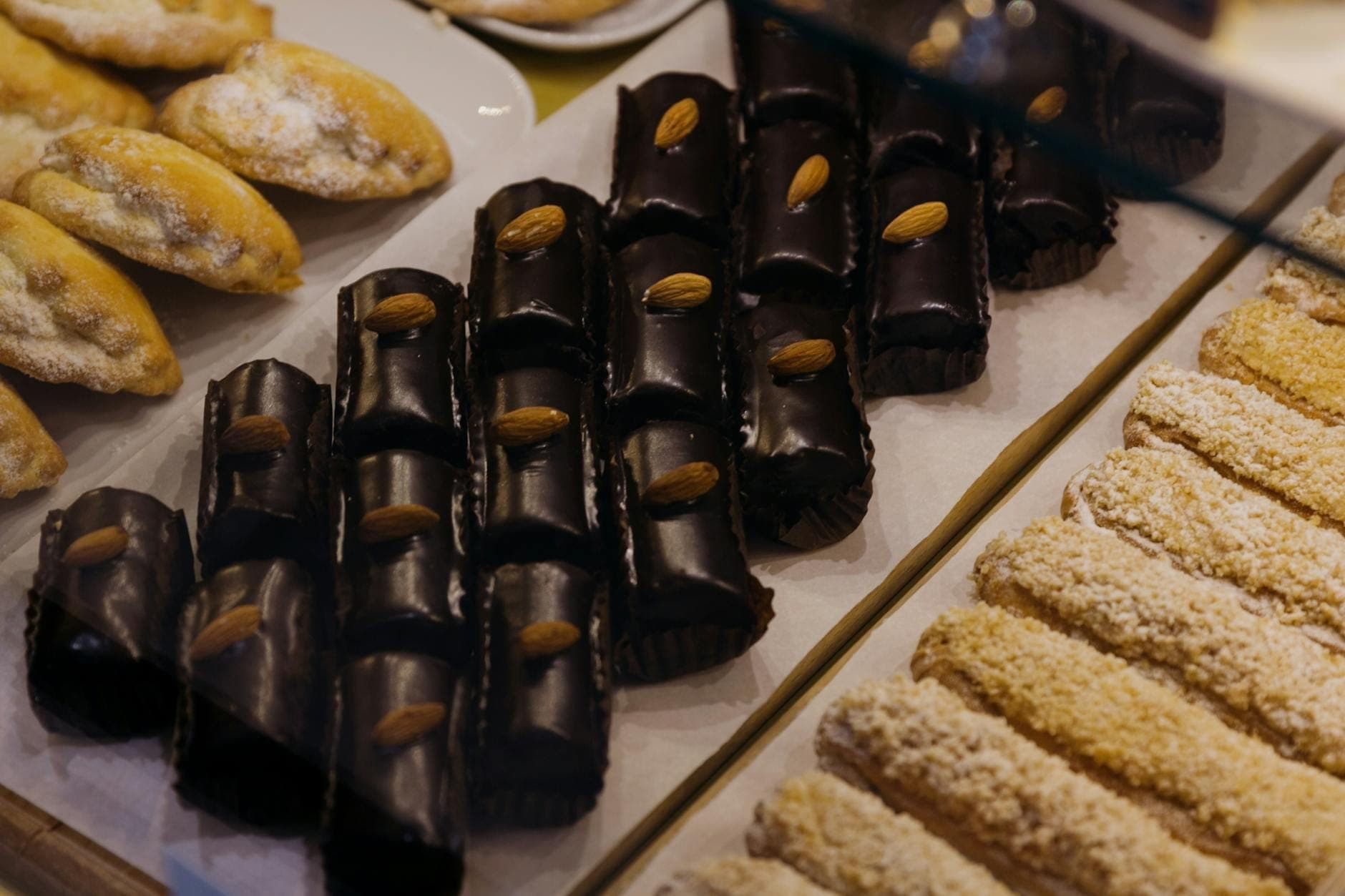Nampan berisi aneka kue khas Sisilia termasuk manisan almond berlapis cokelat dan berbagai dessert Italia tradisional lainnya dalam etalase toko roti.