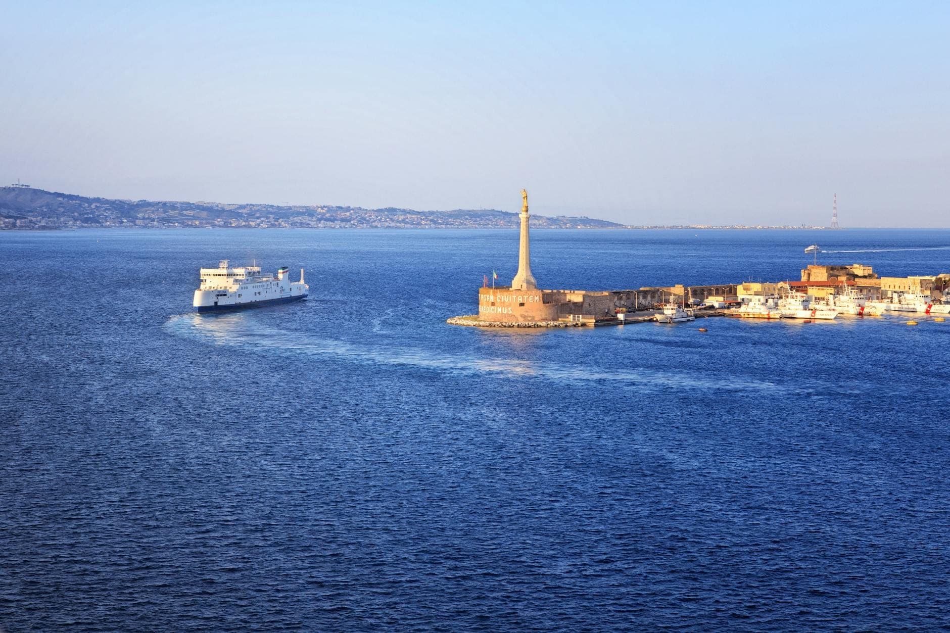 Vista panoramica del mare vicino a Messina, Sicilia, con un traghetto e il prominente punto di riferimento dell'ingresso del porto.