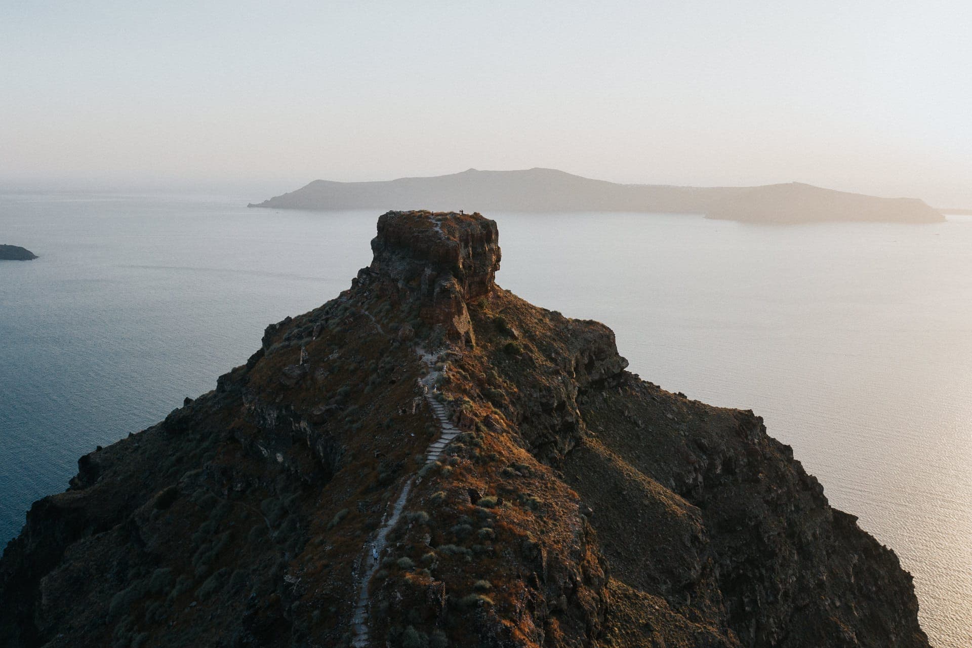 Ein rauer Pfad führt den Skaros Rock in Imerovigli hinauf, der bei Sonnenuntergang auf einer Klippe über dem blauen Wasser der Caldera von Santorini thront.