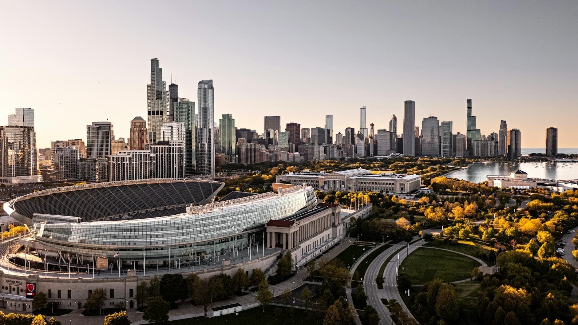 Aerial view of Soldier Field stadium with Chicago skyline and Lake Michigan in the background on a clear day, showing the stadium’s architecture and nearby parkland.
