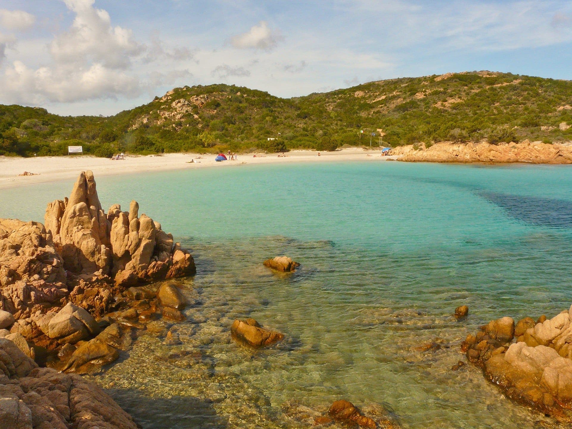 Klares türkisfarbenes Wasser, weißer Sandstrand und einzigartige Granitfelsen an der Spiaggia del Principe mit grünen Hügeln im Hintergrund.
