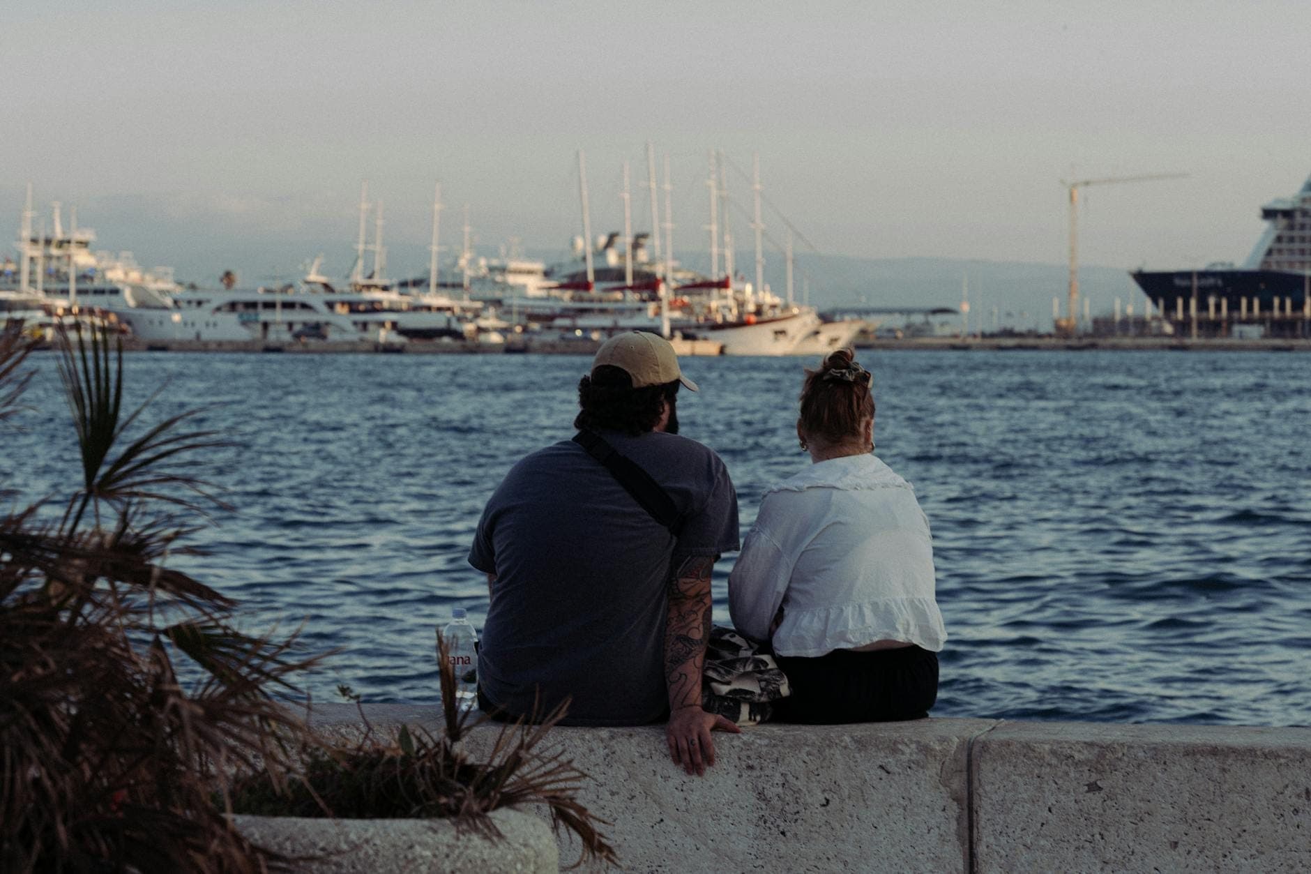 Una coppia seduta insieme sul lungomare di Split, con vista sul mare Adriatico e gli yacht ormeggiati al tramonto.