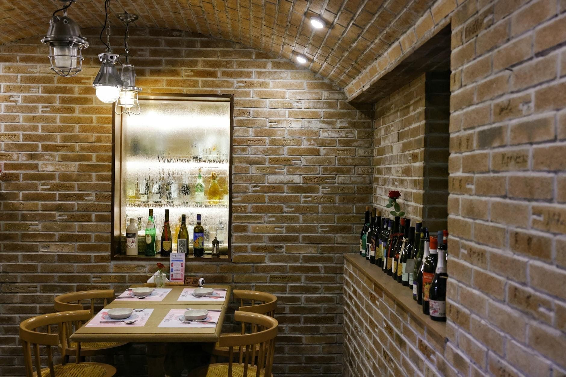 Bar chaleureux aux murs en briques, avec une petite table, des chaises et diverses bouteilles de vin et de spiritueux, évoquant l'atmosphère d'une cave classique de vieille ville européenne.
