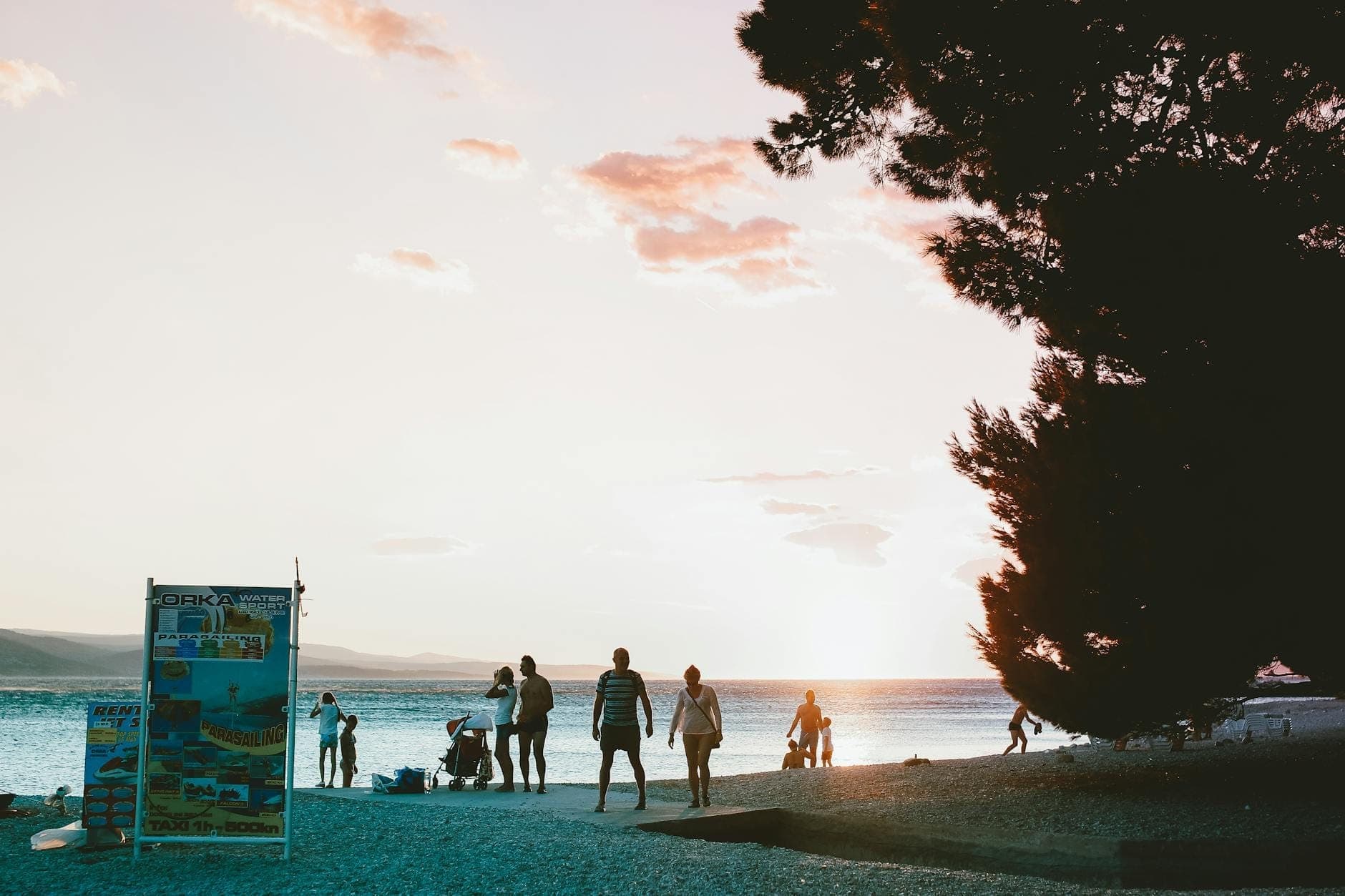 Des personnes se promenant et se relaxant le long du front de mer de Split au coucher du soleil, avec un ciel vibrant et les eaux calmes de l'Adriatique en arrière-plan.